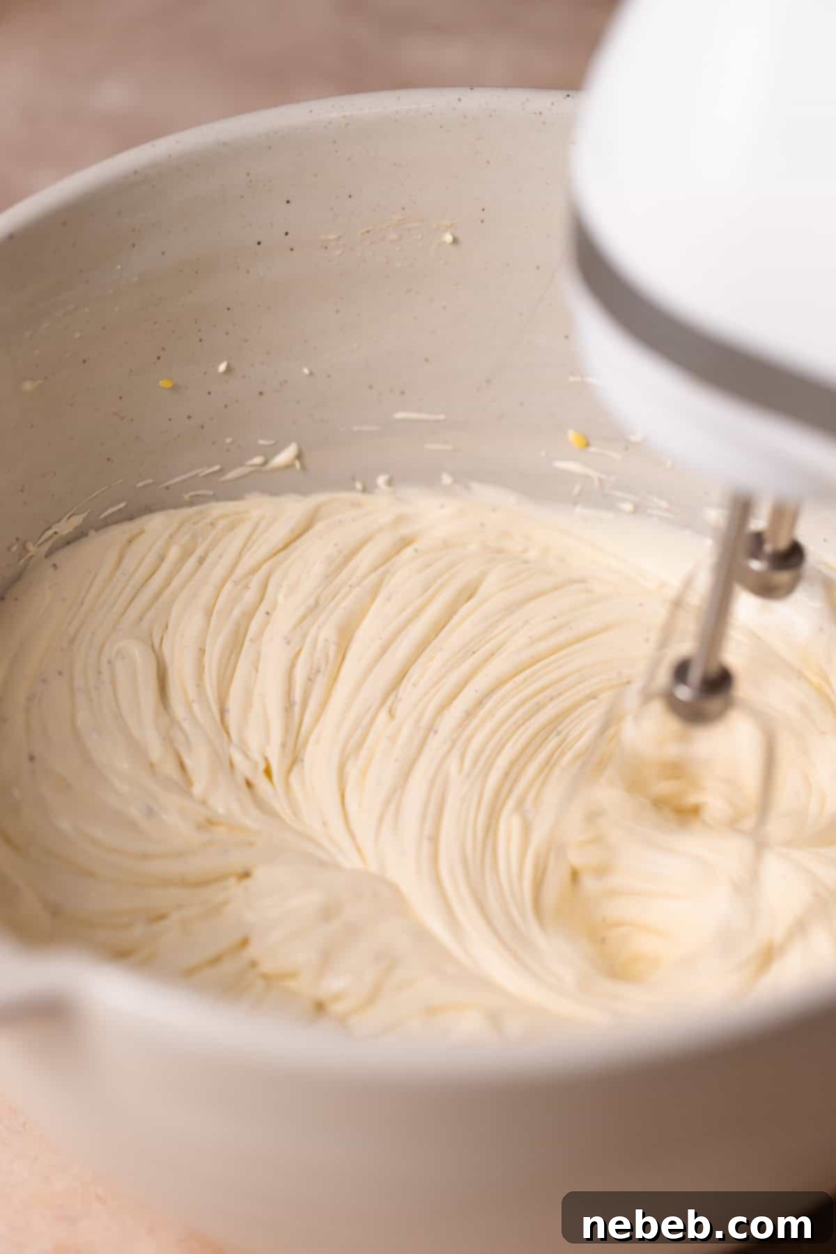 An electric whisk beating the mascarpone filling in a bowl until light and fluffy.