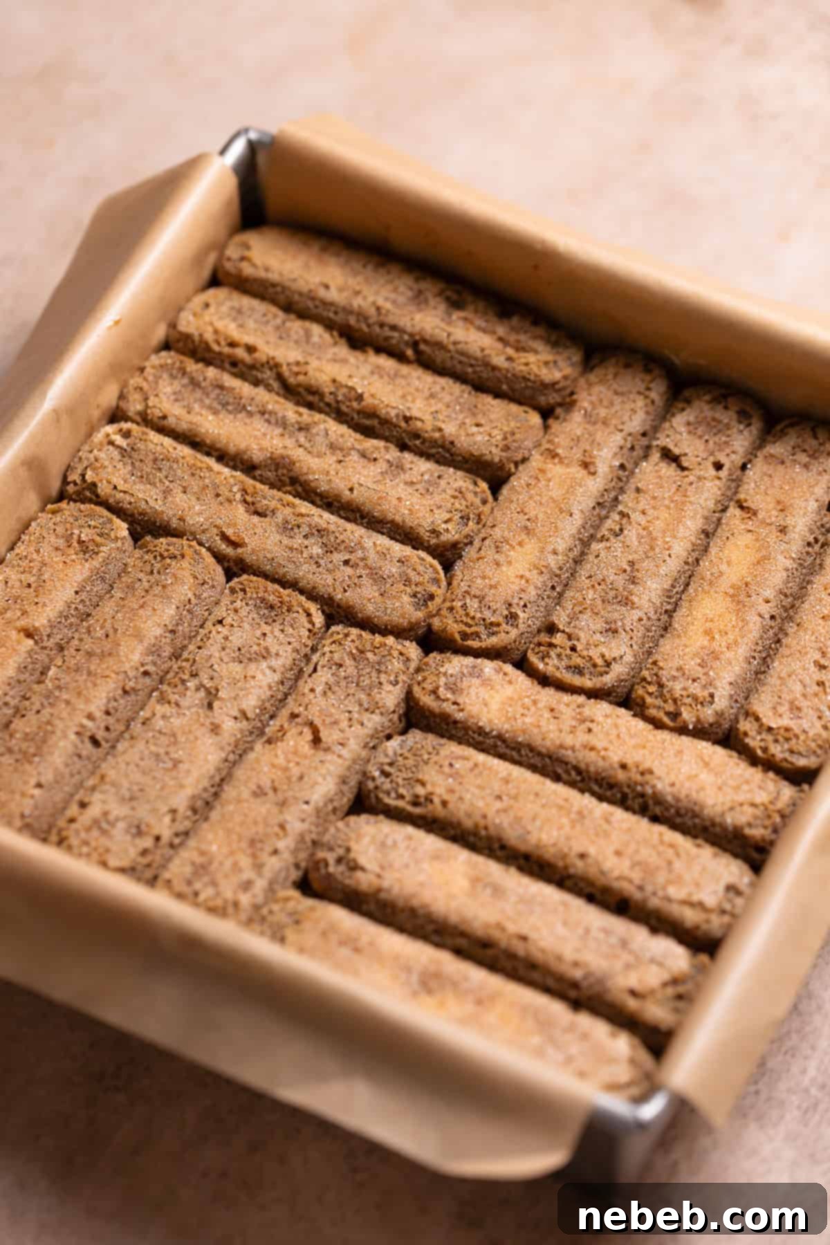 A baking pan showing espresso-soaked ladyfingers carefully arranged on top of a baked brownie layer.
