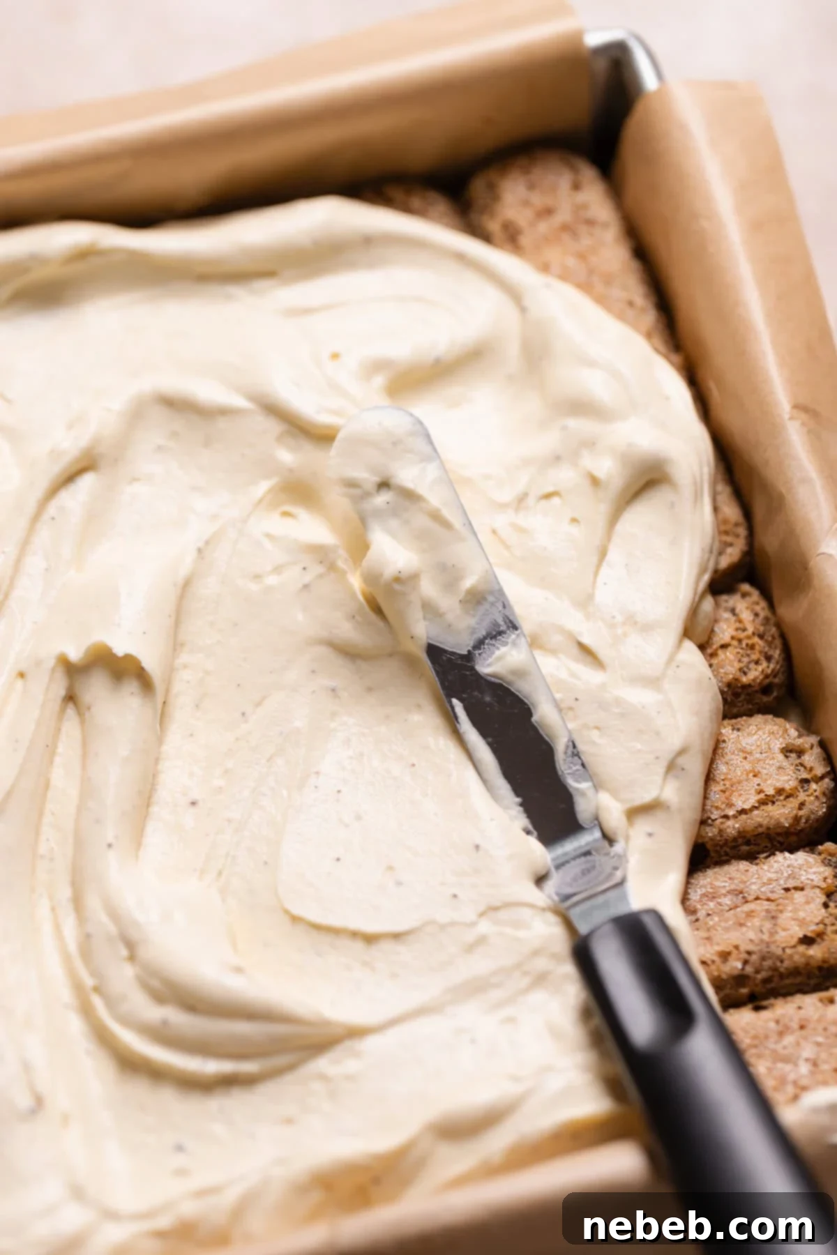 A spatula spreading a layer of creamy mascarpone filling over espresso-soaked ladyfingers on top of brownies.