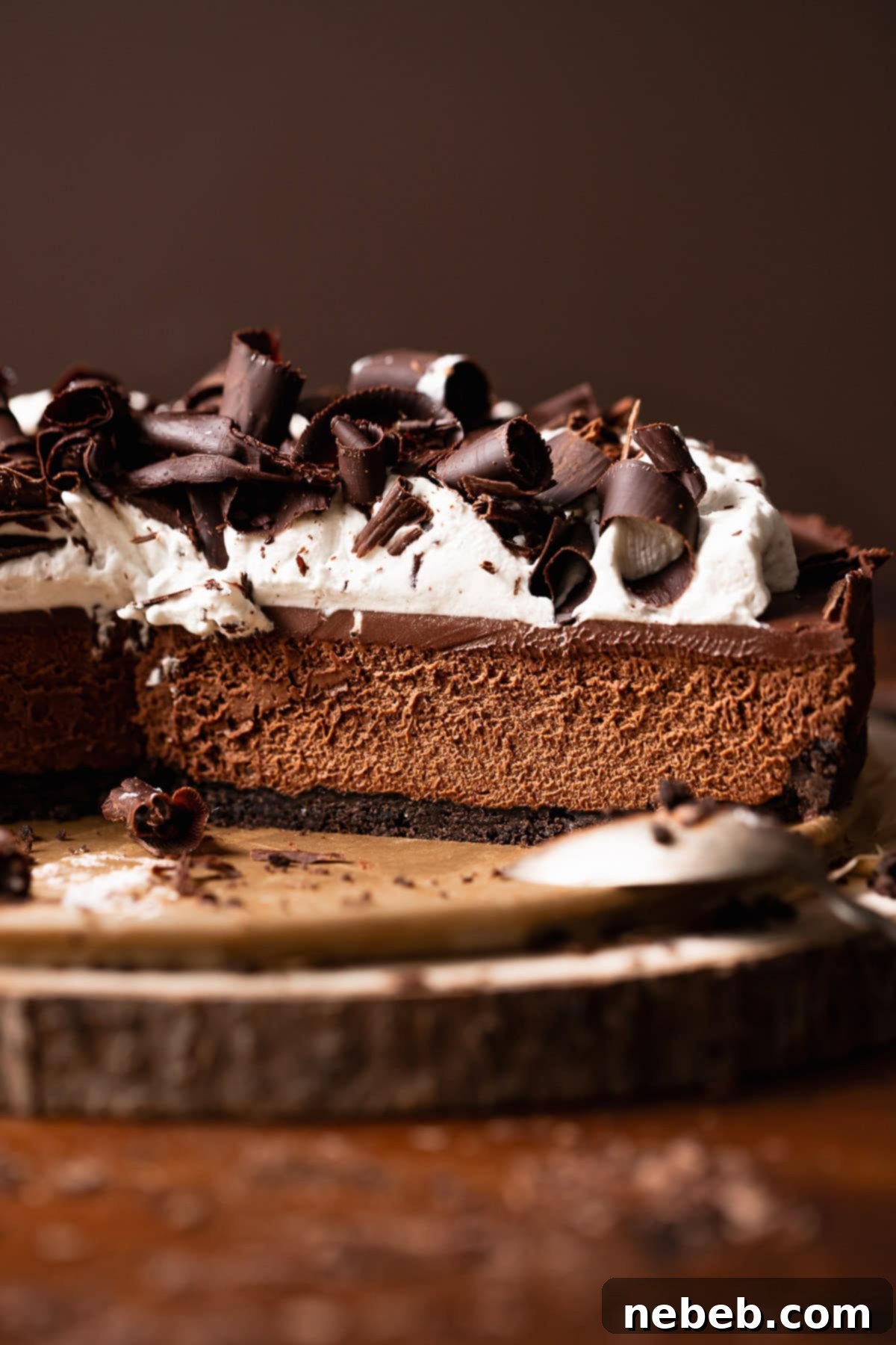 A stunning dark chocolate mousse pie with slices missing, revealing its layers of Oreo crust, rich mousse, and ganache, topped with whipped cream and chocolate curls, presented on a rustic wooden platter.