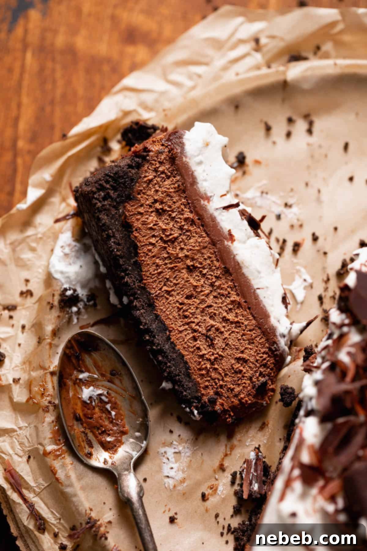 A perfect slice of dark chocolate mousse pie, showcasing the layers of rich mousse, glossy ganache, fluffy whipped cream, and the sturdy Oreo crust, served on brown parchment paper.