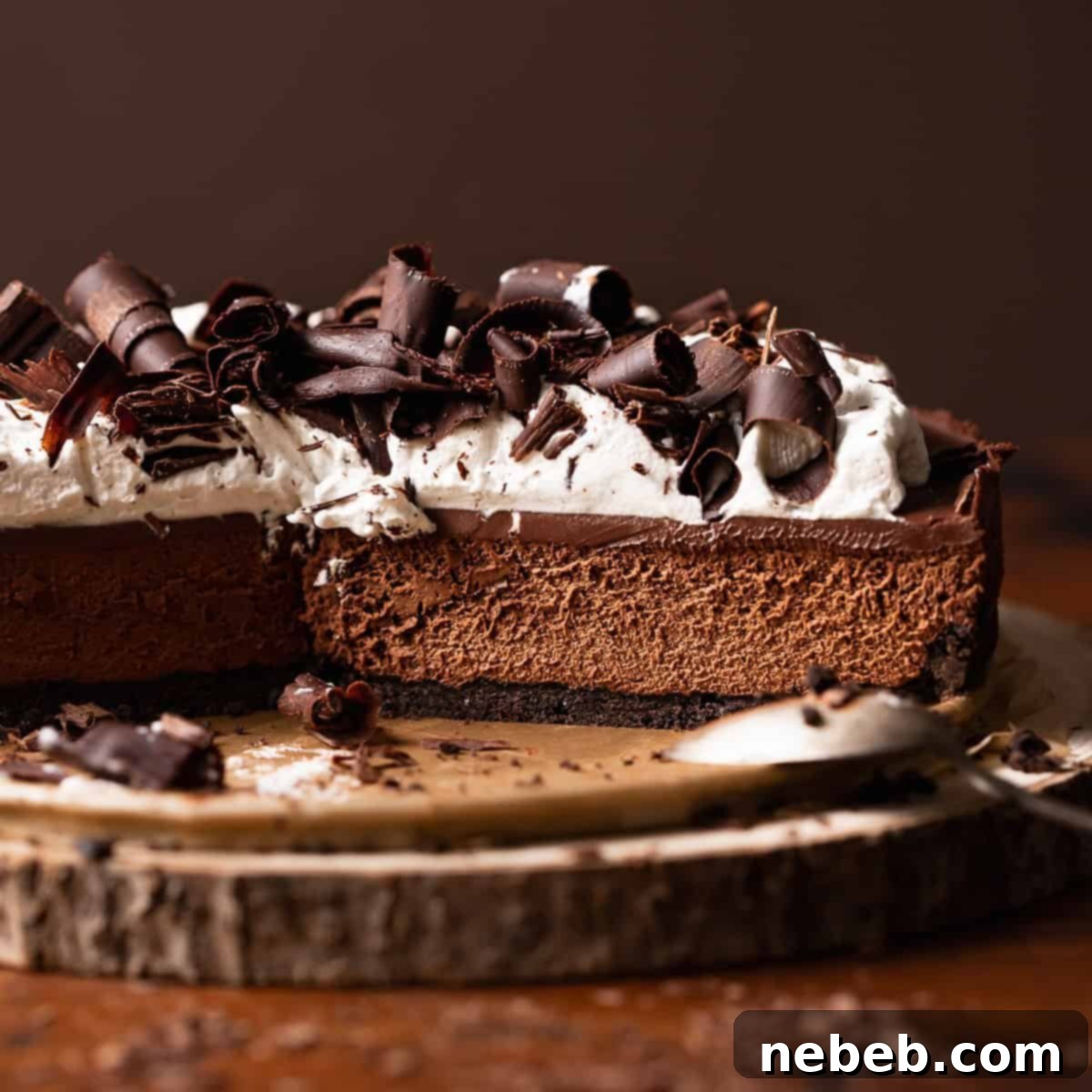A luxurious chocolate mousse pie with an Oreo crust, topped with homemade whipped cream and delicate chocolate shavings, sitting on a wooden platter.