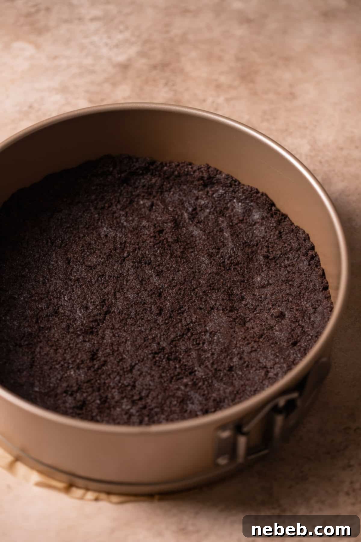 Buttery Oreo cookie crumbs pressed into a 9-inch springform cake pan, ready for baking.