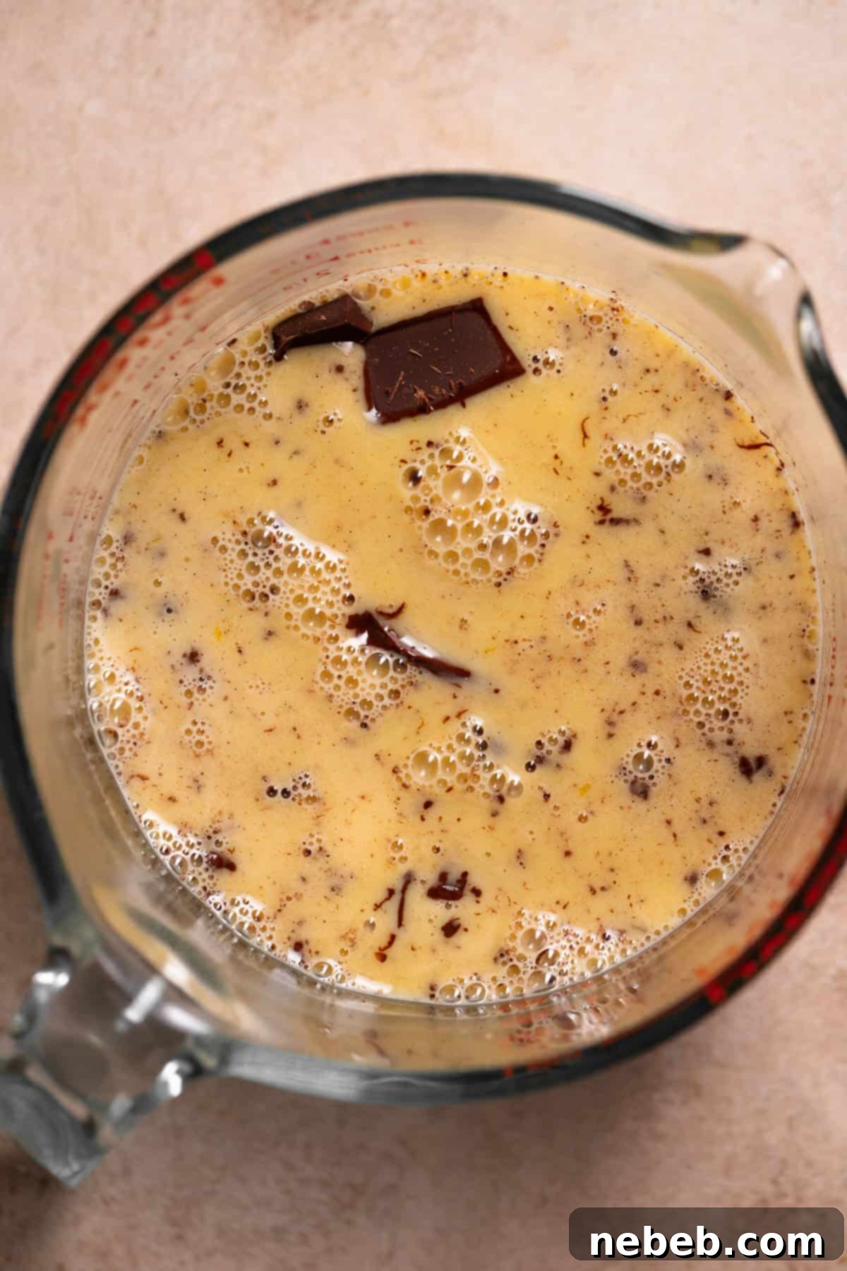 Hot egg-cream mixture being poured over finely chopped dark chocolate and bloomed gelatin in a bowl, preparing to form the silky ganache base for the mousse.