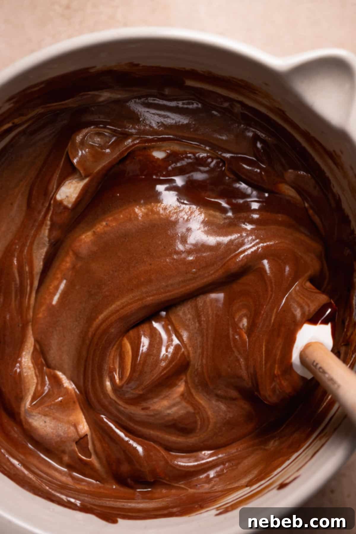 A spatula gently folding the rich chocolate ganache base into the fluffy whipped cream, creating the airy mousse filling.