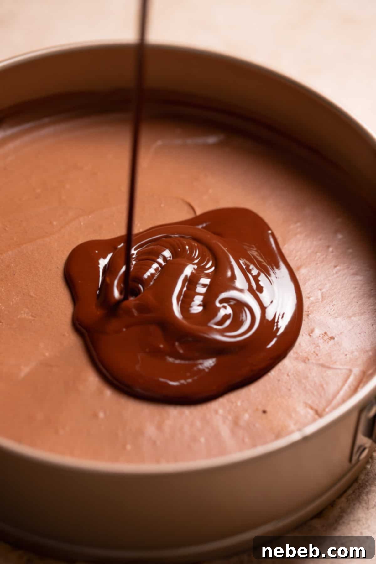 Smooth, glossy chocolate ganache being poured evenly over the fully set dark chocolate mousse layer in the pie.