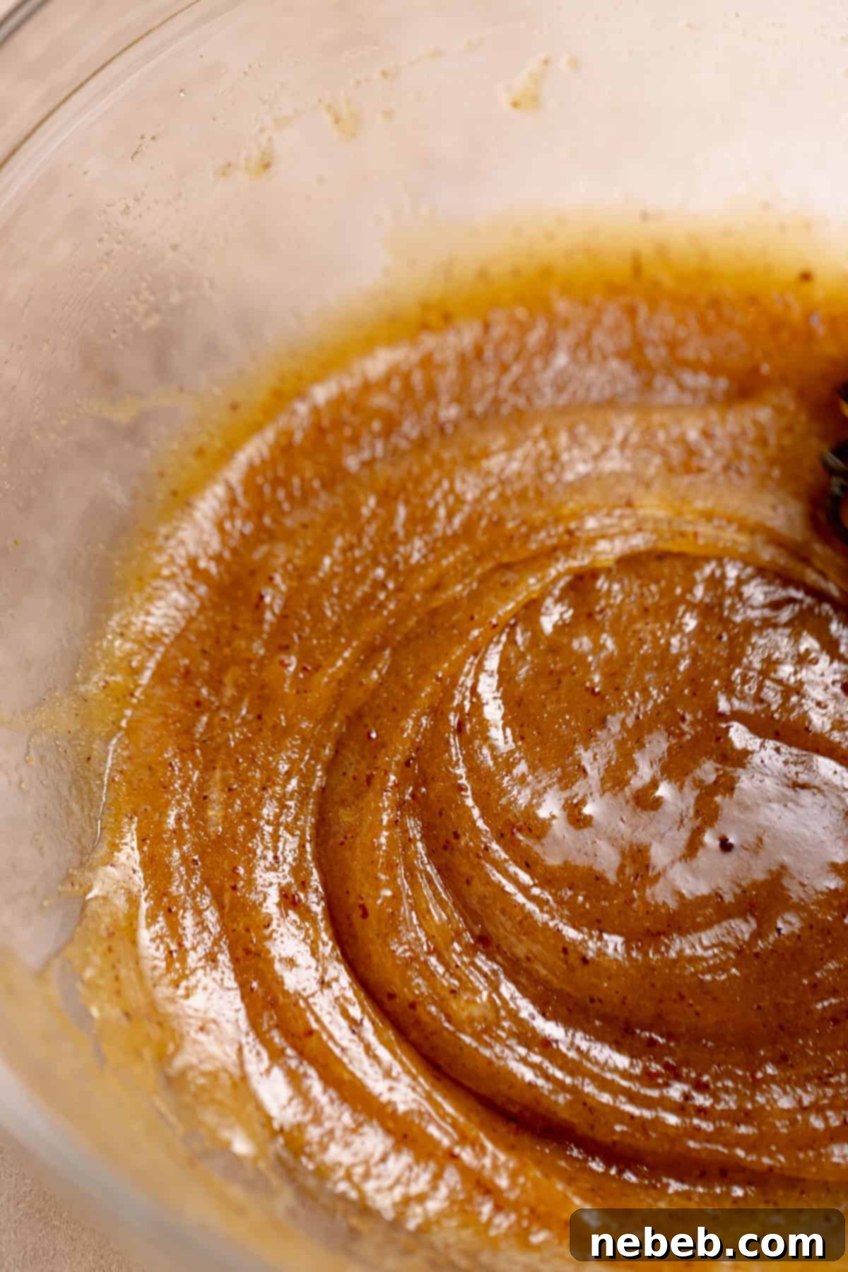 A glass bowl with the brown butter, sugar, and eggs being whisked together.
