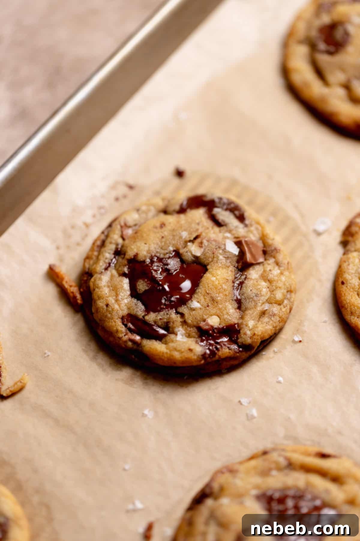 A brown butter cookie on a tray after baking sprinkled with flaky sea salt.
