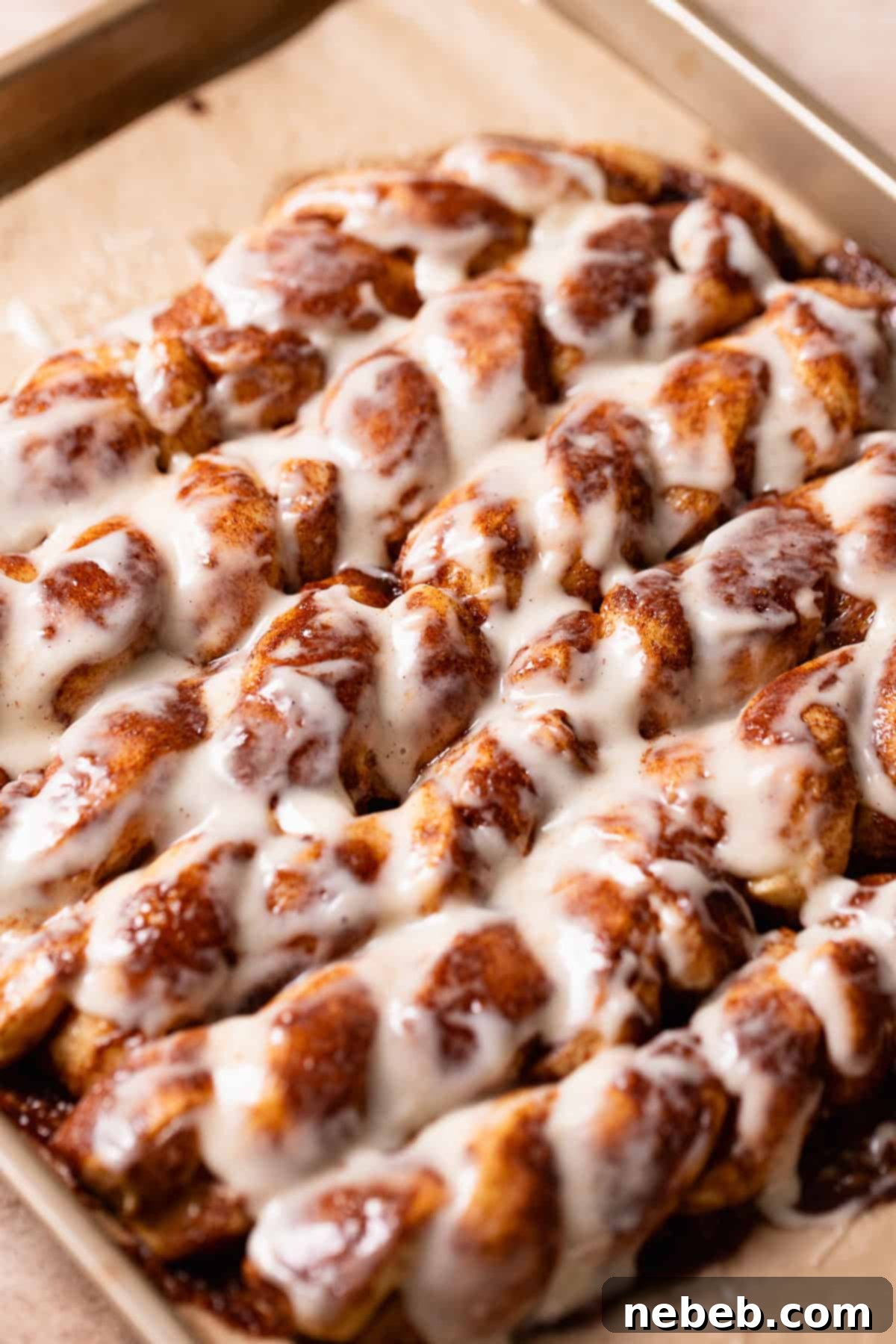 Cinnamon roll twists covered in cream cheese icing on a baking tray.