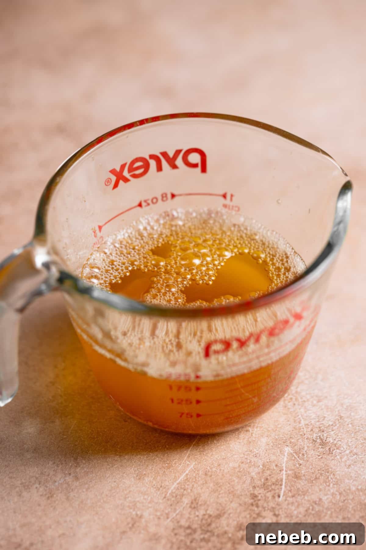 A glass measuring cup full of liquid brown butter, showing golden brown milk solids.