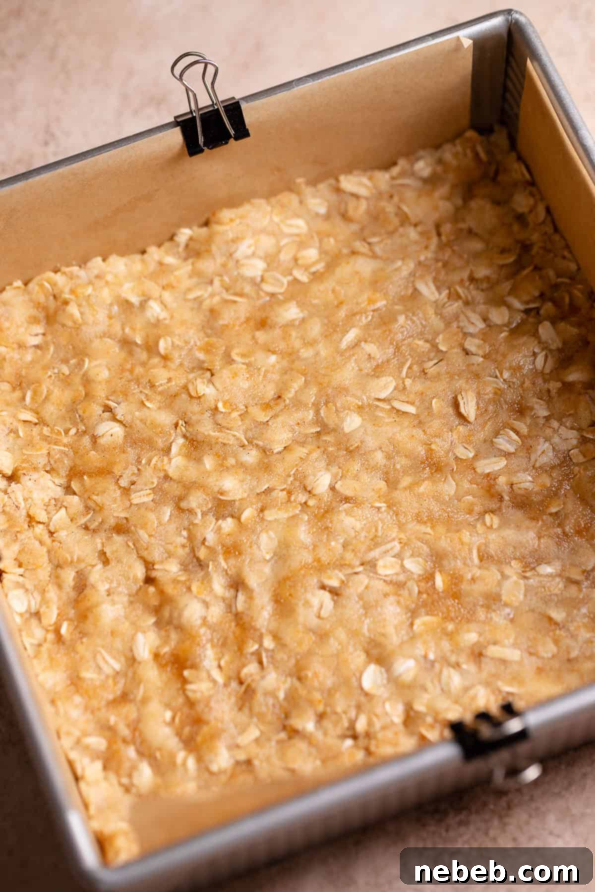 Brown sugar oatmeal crumble dough pressed into the bottom of a parchment-lined baking pan.