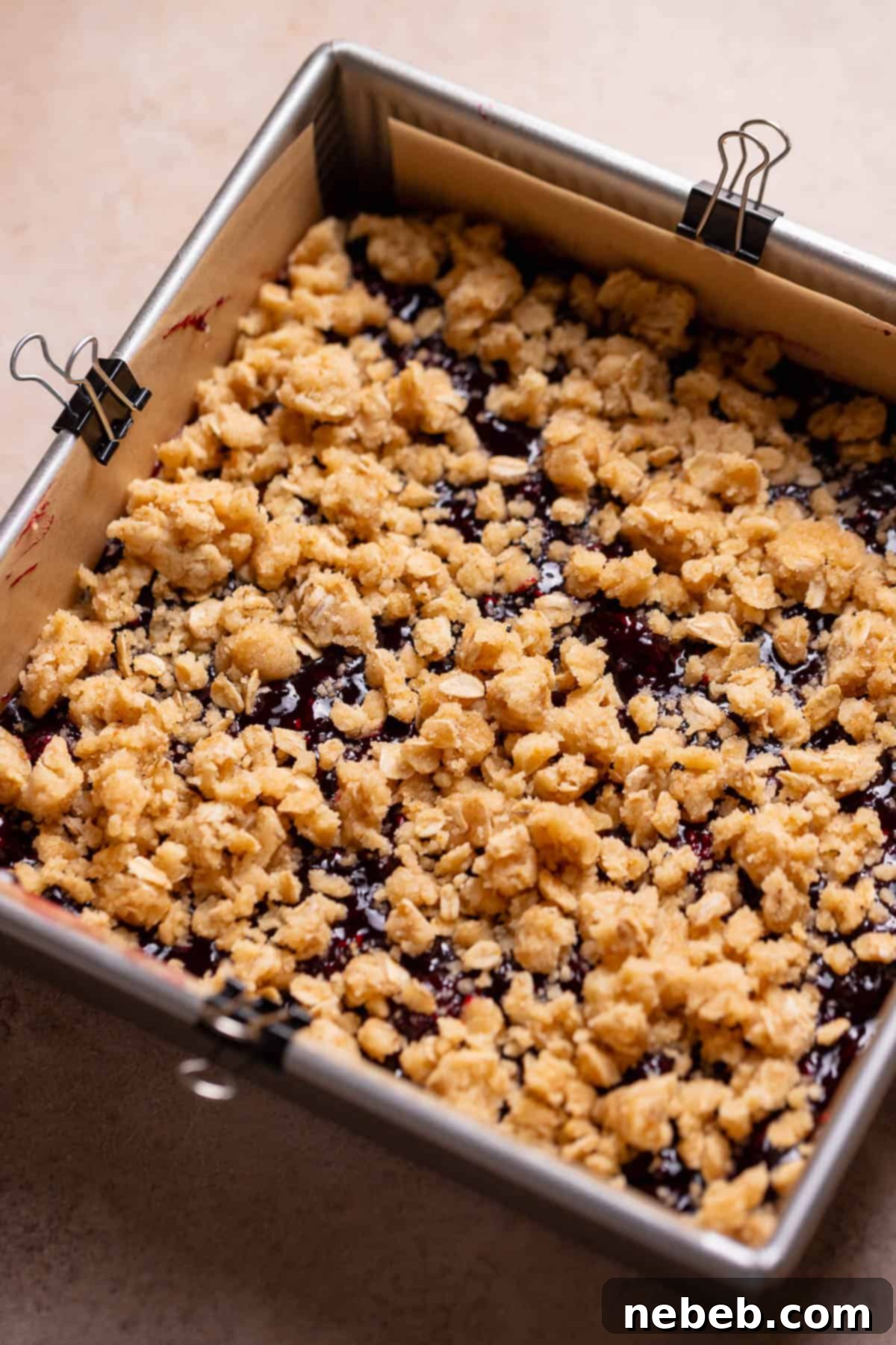 Berry crumb bars in a pan before baking, showing the berry layer and crumb topping.
