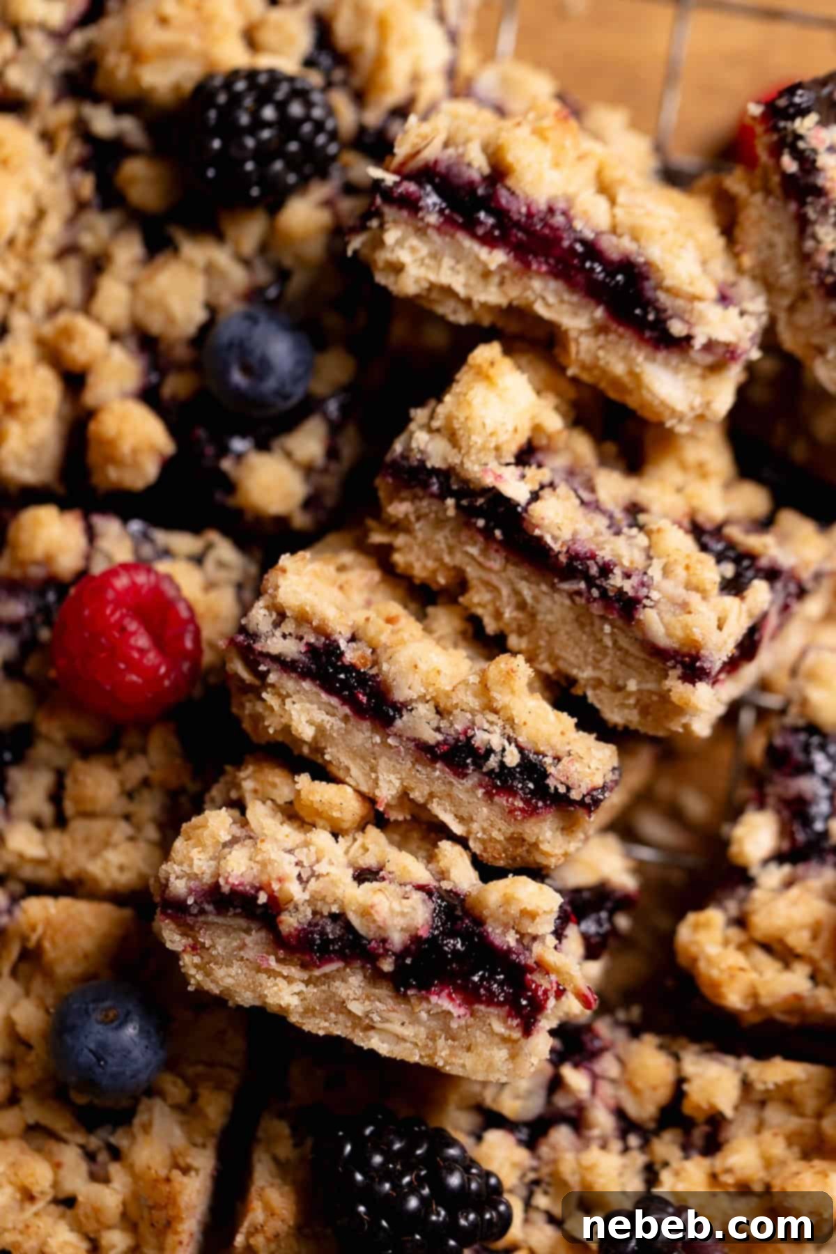 Four fruit crumble bars stacked on their sides, revealing the thick, jammy fruit-filled centers and the distinct layers of crumble.