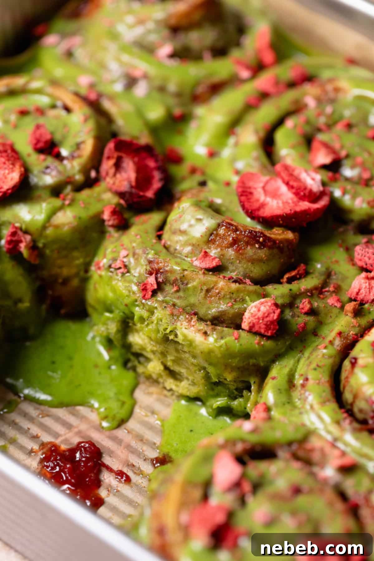 Matcha cinnamon rolls in a baking pan, topped with green glaze and freeze-dried strawberries.
