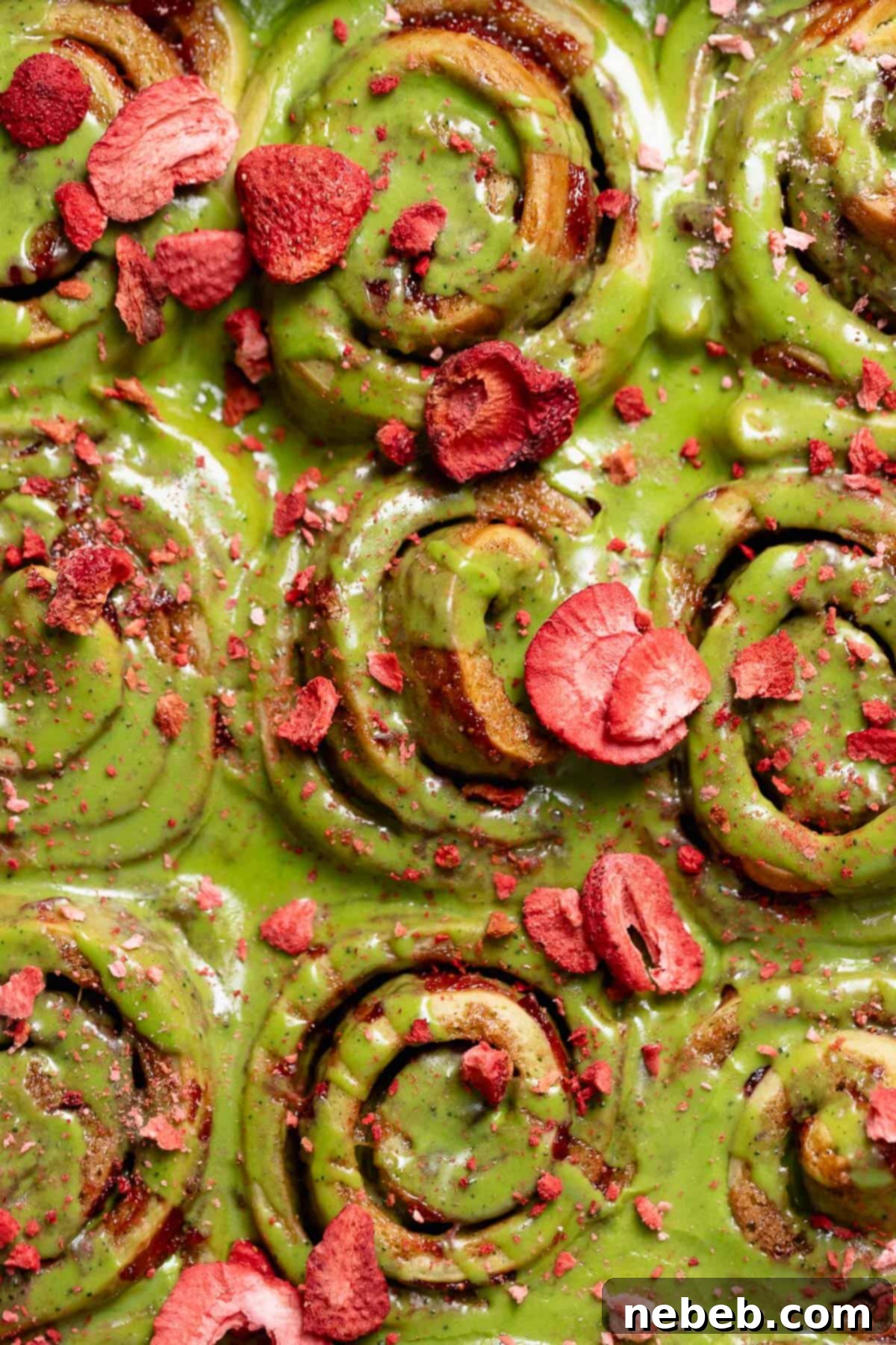 Close-up of baked matcha cinnamon rolls with strawberry filling and a vibrant matcha glaze, garnished with freeze-dried strawberries.