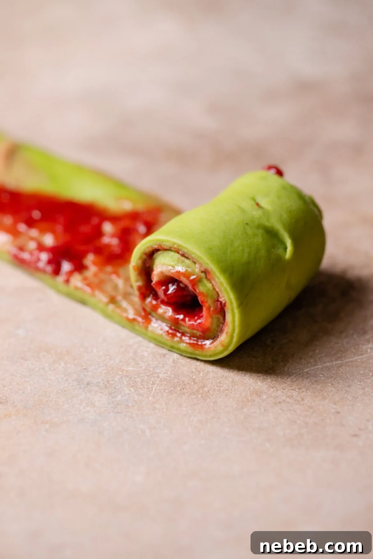 A strip of dough being carefully rolled into a neat cinnamon roll spiral.