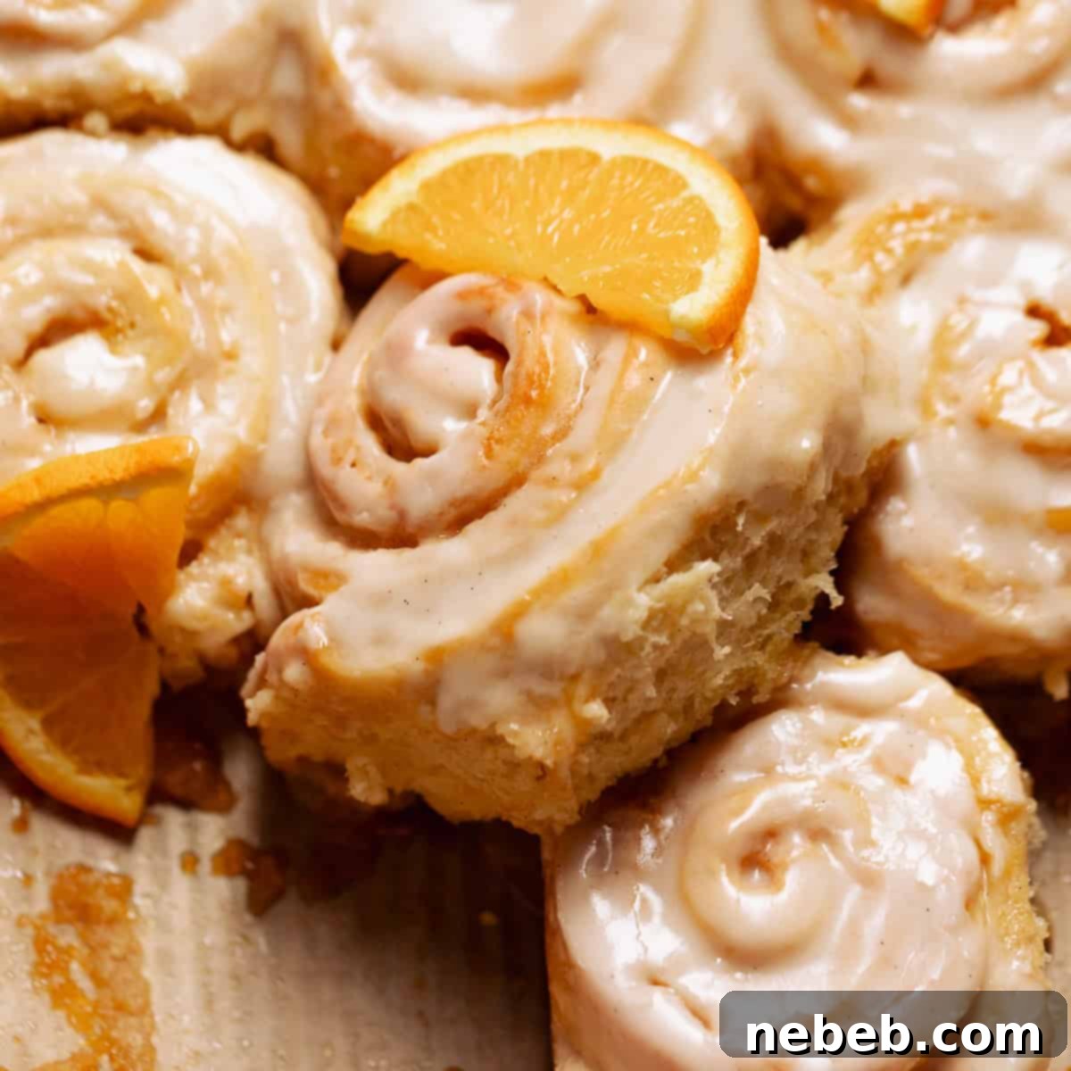 Orange cinnamon rolls in a baking pan with fresh orange slices on top.
