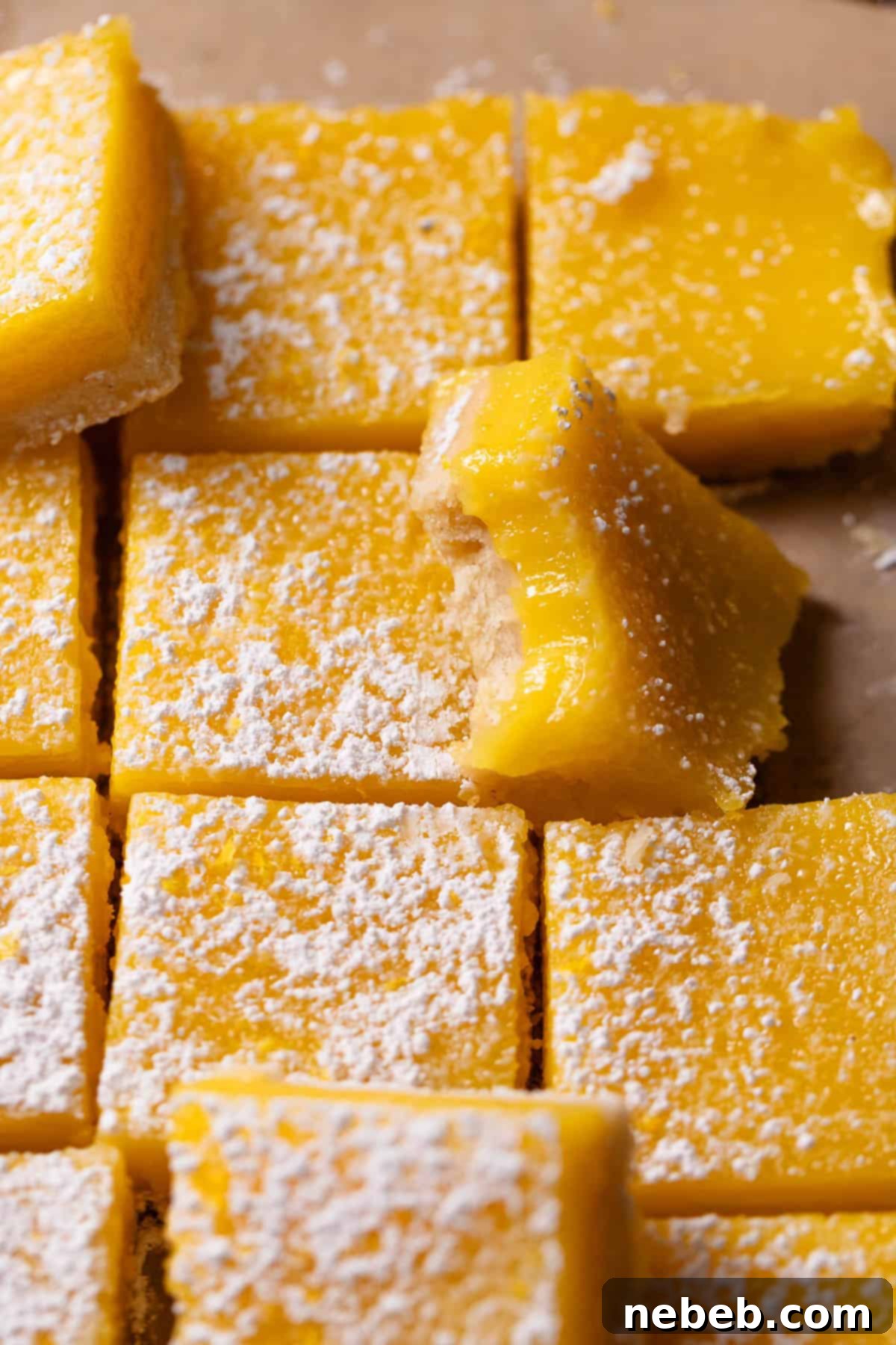 Lemon bars dusted with powdered sugar with one missing a bite, showcasing the golden shortbread and creamy lemon layer.