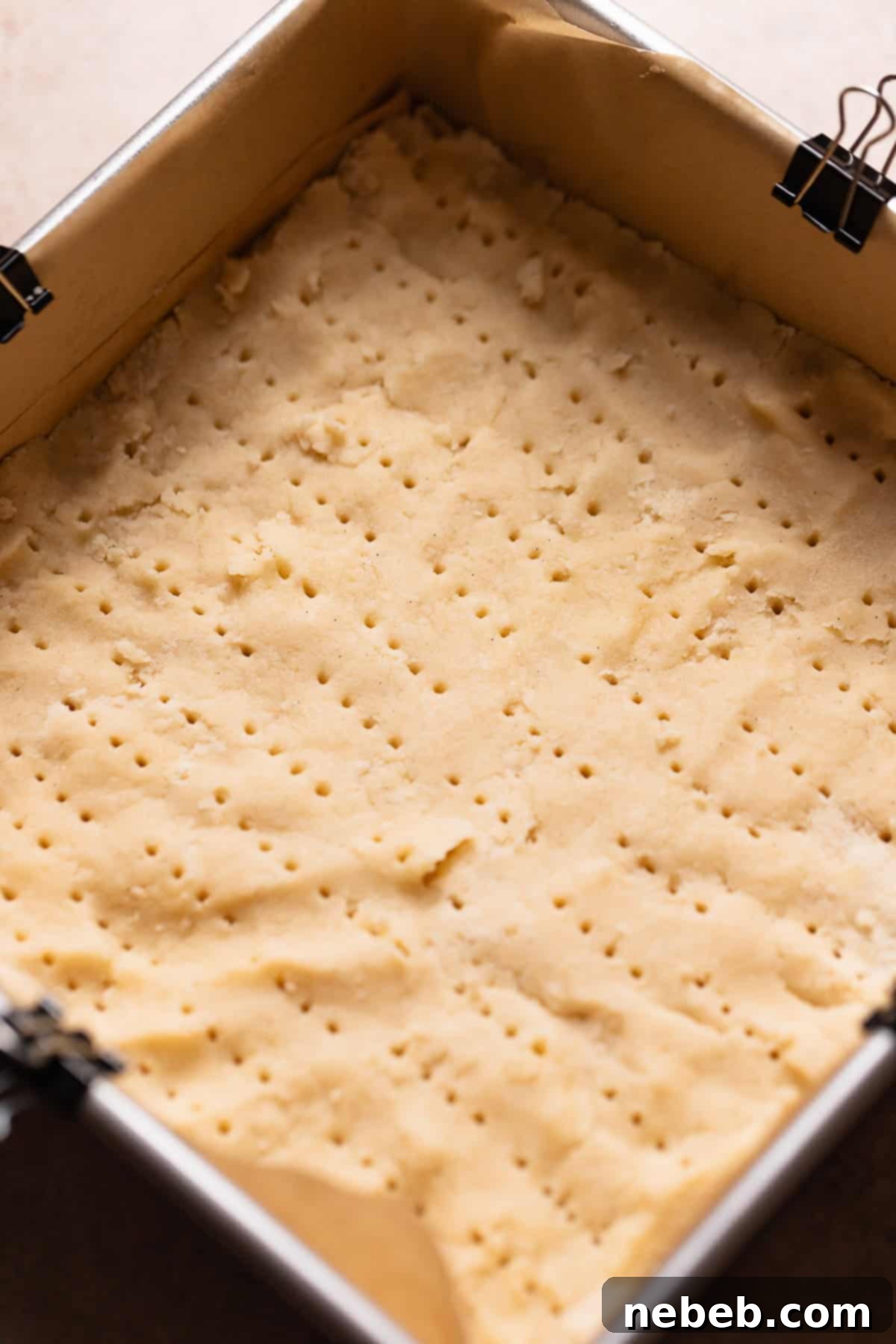 Shortbread dough evenly pressed into an 8x8 square pan and pricked with a fork before its initial bake.