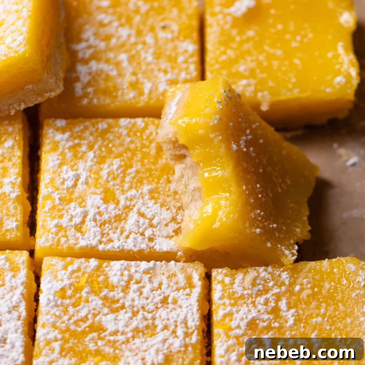 Lemon bars dusted with powdered sugar with one missing a bite, showing the vibrant lemon curd and shortbread crust.