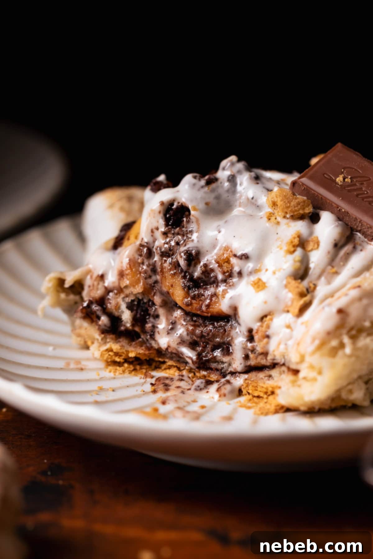 A smores roll on a white plate with bites missing to show the gooey texture, highlighting the chocolate, graham cracker, and marshmallow layers.