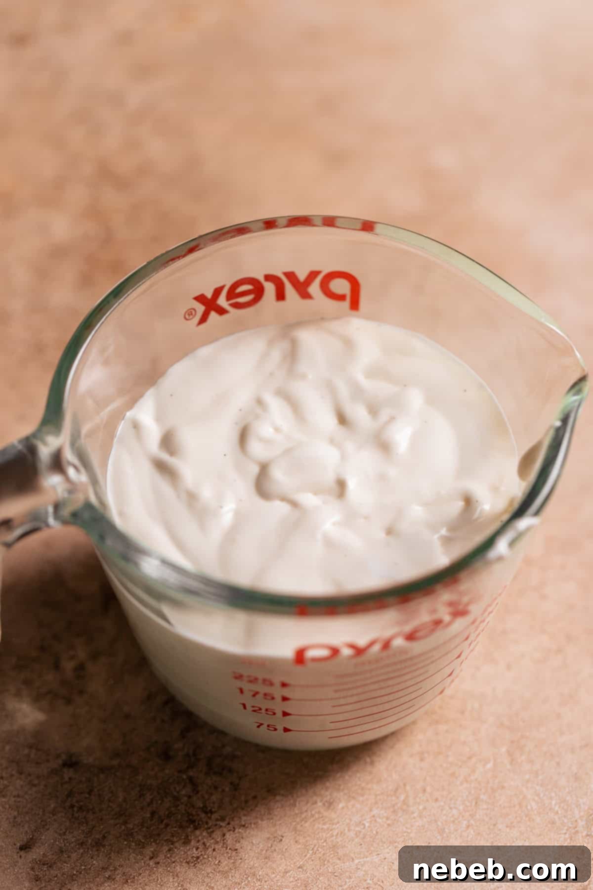 A glass measuring cup full of fluffy marshmallow glaze, ready to be poured over the warm rolls.