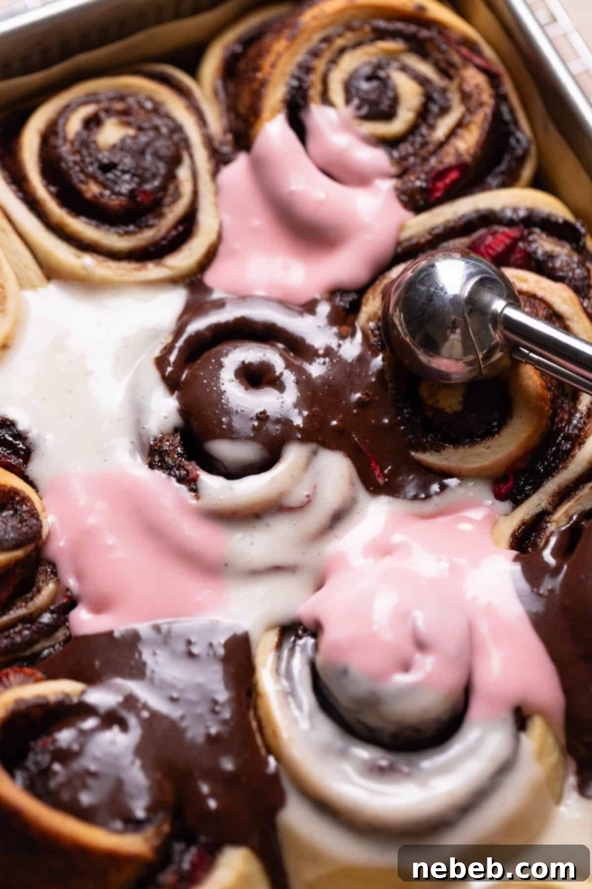 A scoop alternating the three icing colors on top of the baked cinnamon rolls, creating a beautiful marbled effect.