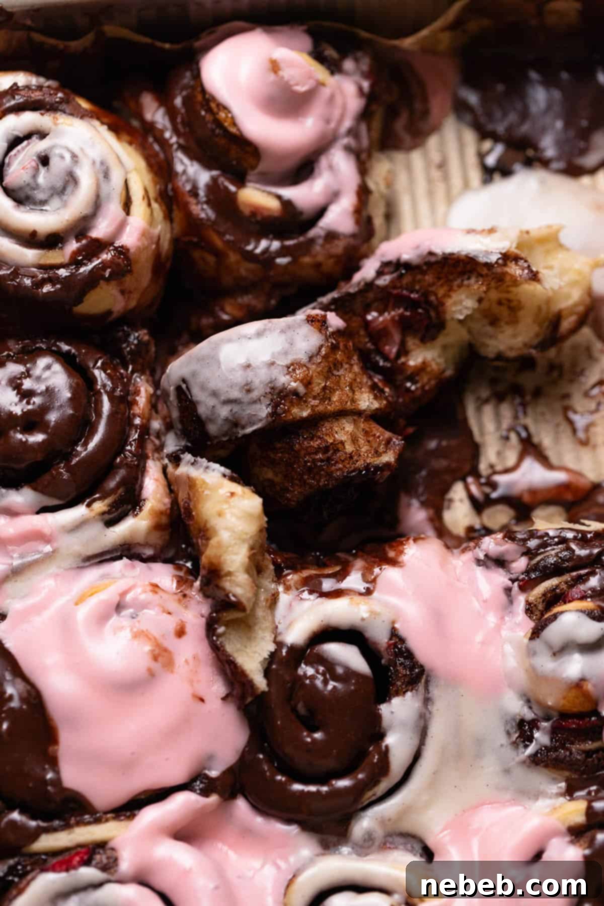 A cinnamon roll half unrolled in the baking pan to show the gooey chocolate-strawberry center of the Neapolitan roll.