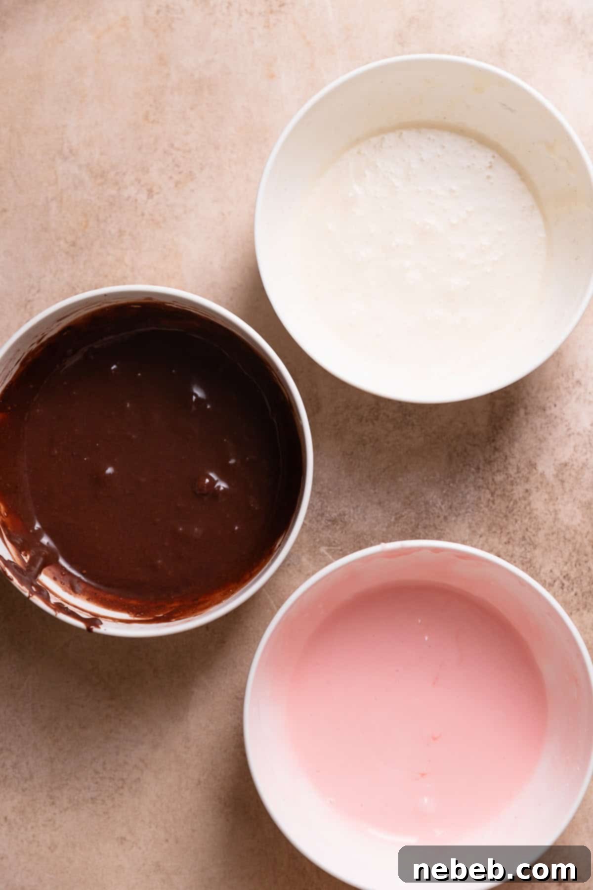 Three bowls of icing with chocolate, strawberry, and vanilla flavors, for the tri-colored Neapolitan topping.