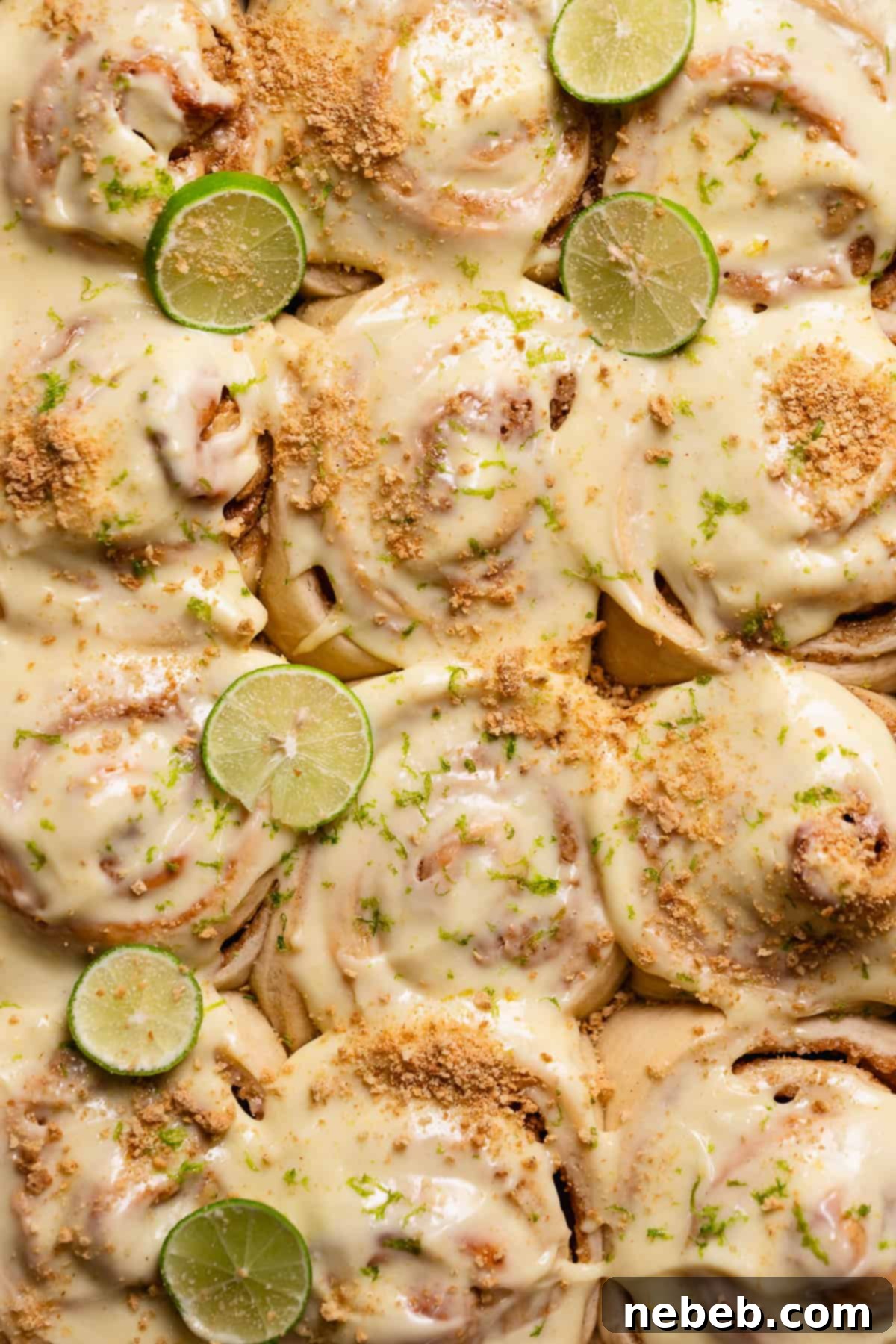 Key lime pie rolls with cream cheese frosting, key limes, and graham cracker crumbs on top.