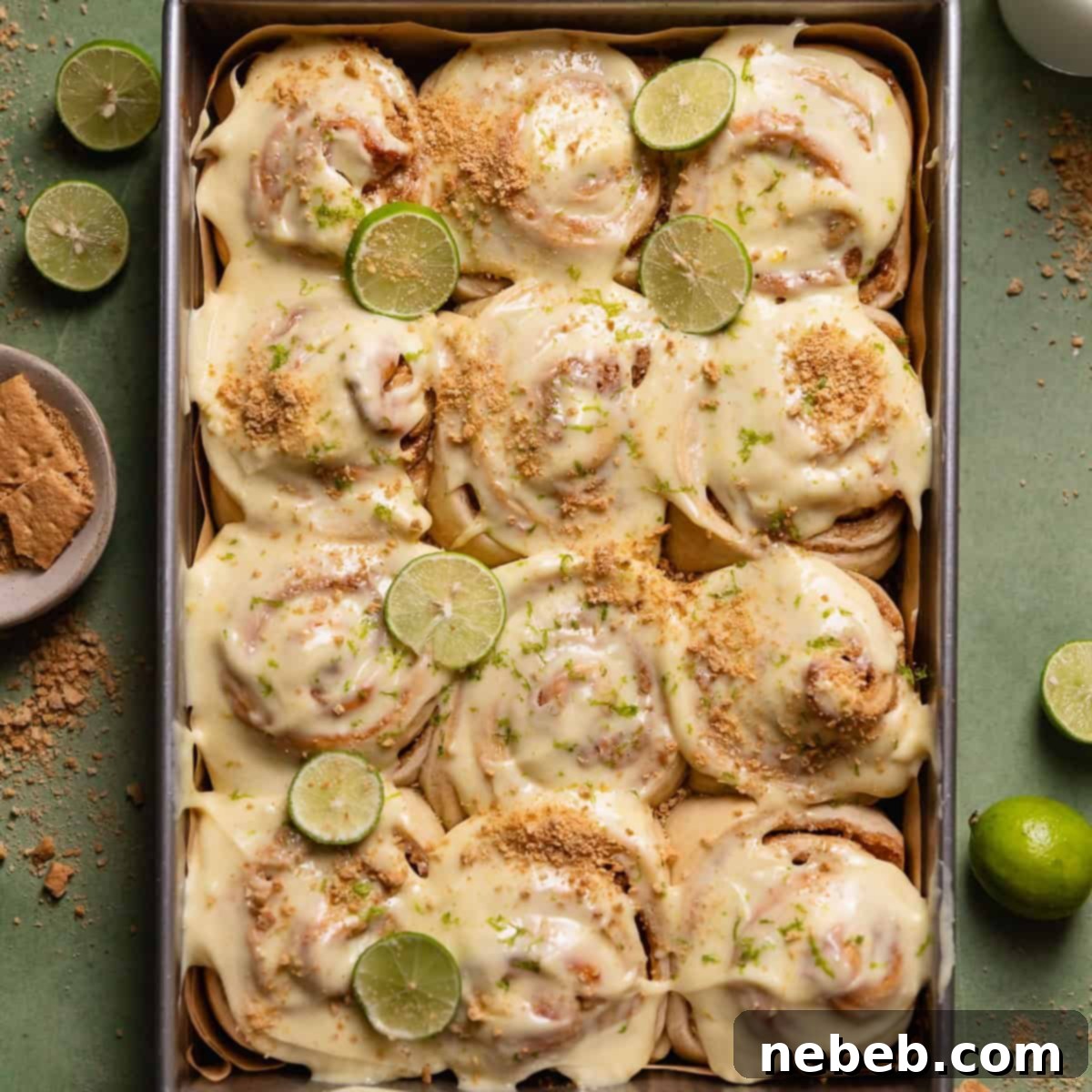 Key lime cinnamon rolls in a baking pan with key limes and graham crackers on top.