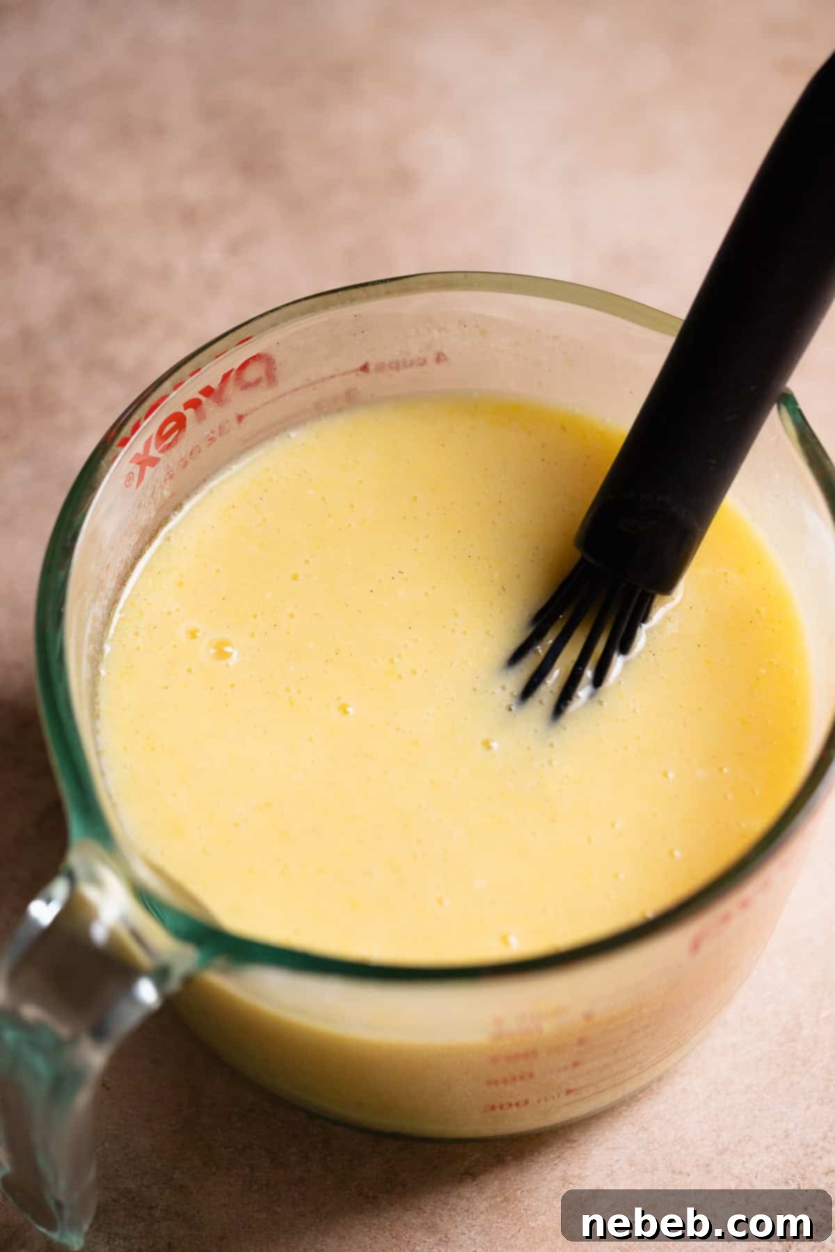 Wet ingredients whisked together in a glass measuring cup, showing buttermilk, sugar, eggs, oil, sour cream, and vanilla.