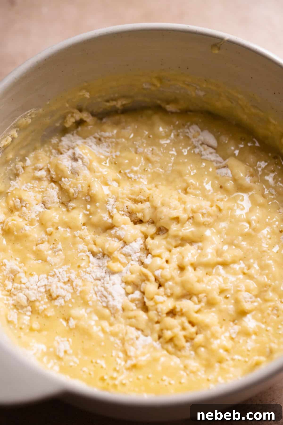 The whisked wet and dry ingredient batter in a bowl with some flour streaks remaining, indicating proper mixing.