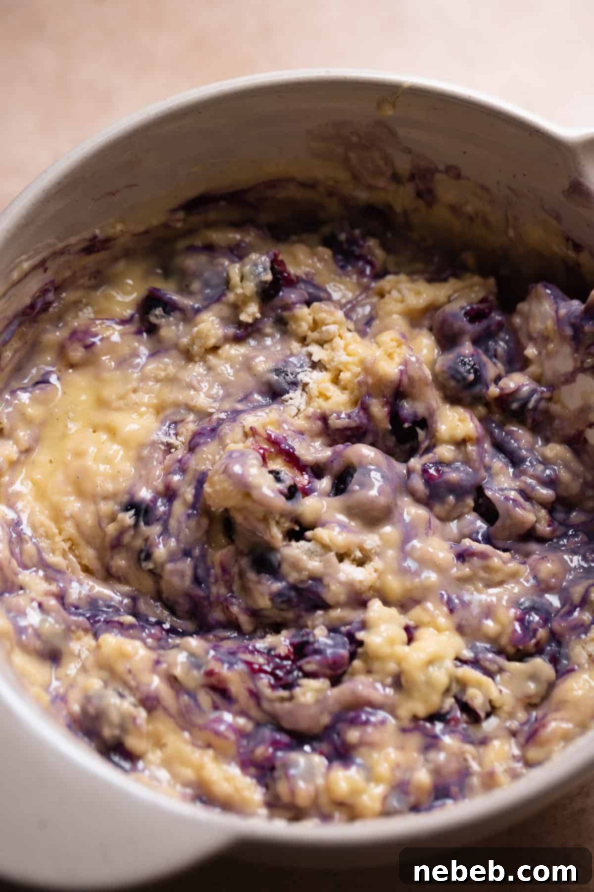 Blueberry muffin batter in a mixing bowl with frozen blueberries gently folded in.