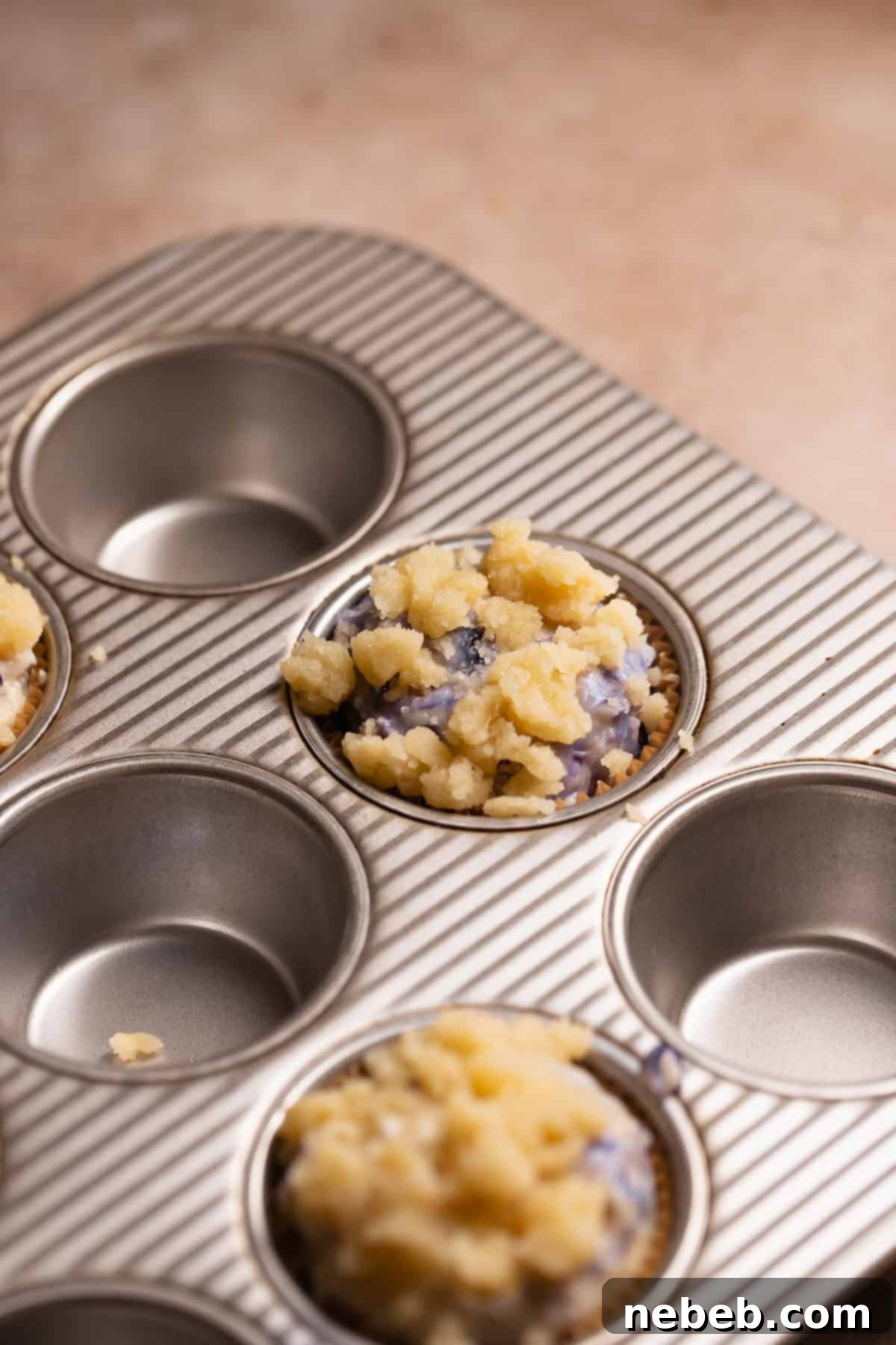 Blueberry muffin batter scooped into a muffin pan and generously topped with crumbs.