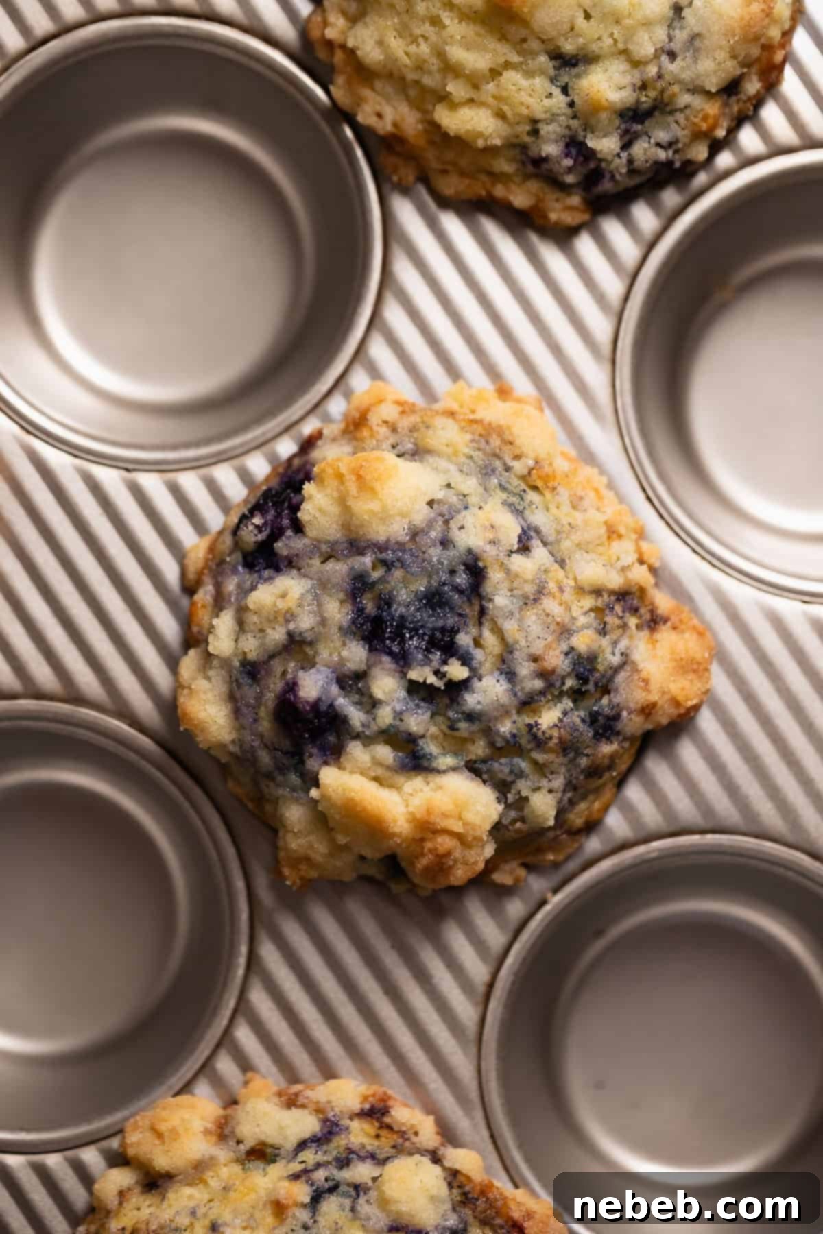 Freshly baked blueberry muffins with crumb topping in a muffin pan, golden brown.
