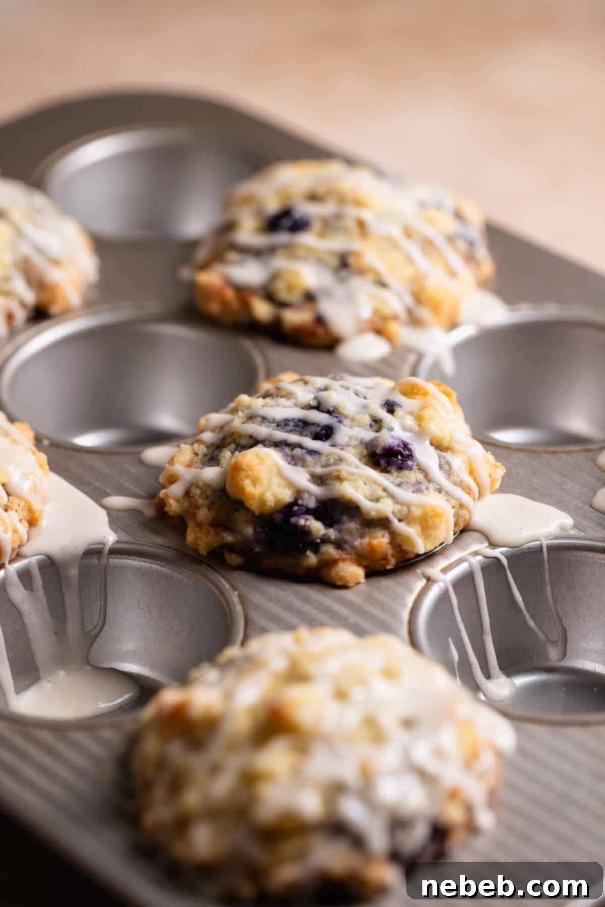 Warm muffins in a baking pan being drizzled with sweet vanilla glaze.