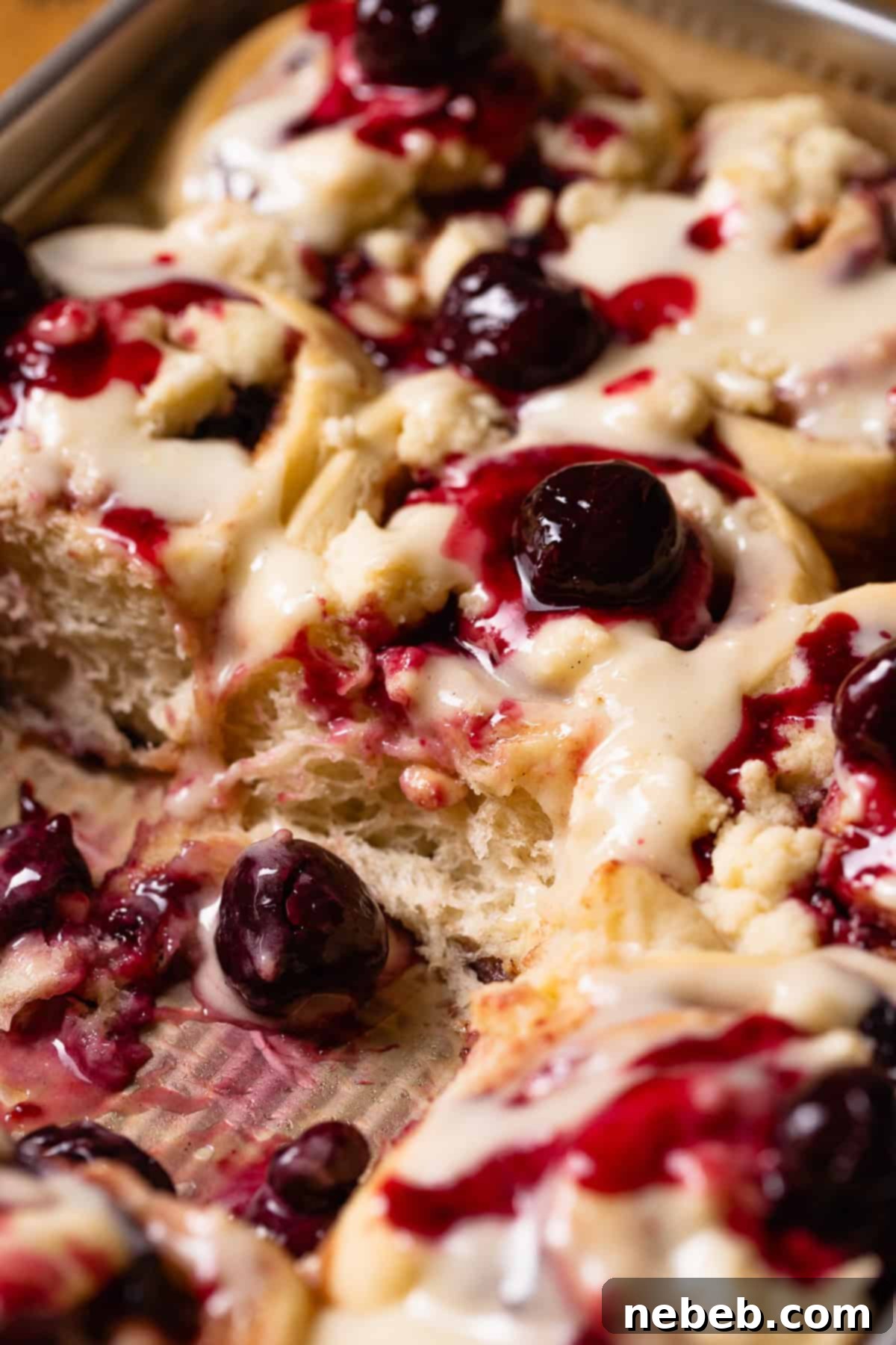 Cherry pie cinnamon rolls in a baking pan, swirled with cherry filling and topped with pie crumb.