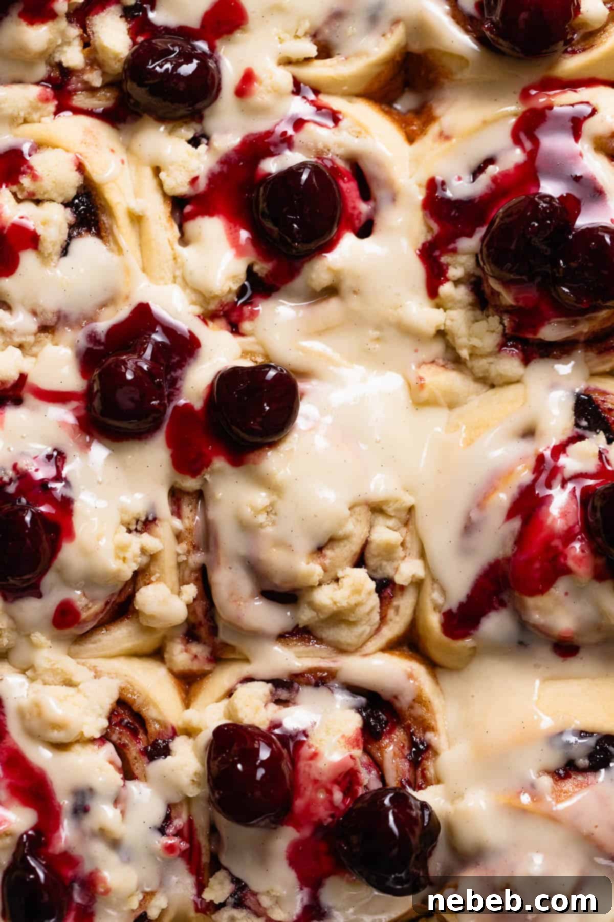 Overhead view of cherry cinnamon rolls in a baking pan topped with cream cheese frosting and swirled with juicy cooked cherries.