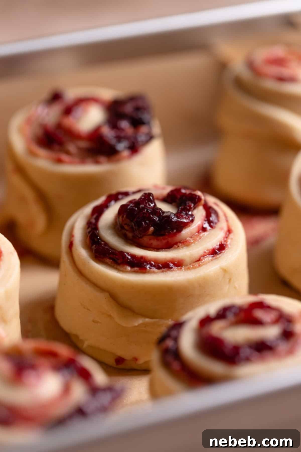 A close up view of an unbaked cherry cinnamon roll in a baking pan.