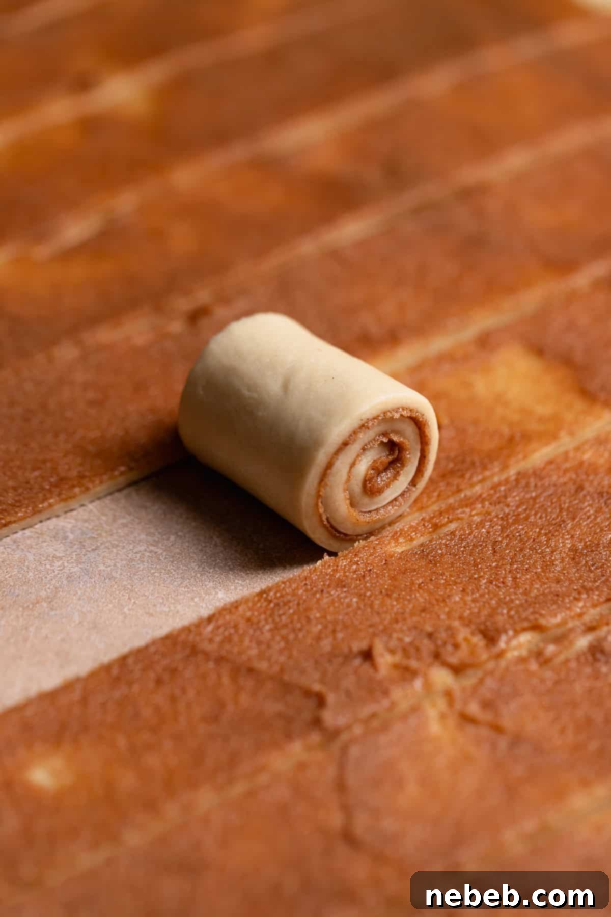 A cinnamon roll strip being rolled up.