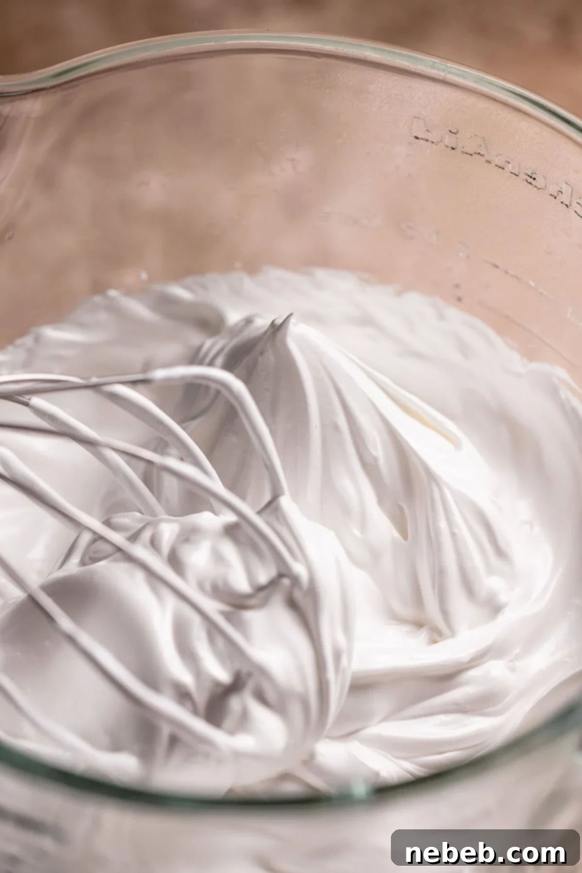 Italian meringue frosting with stiff peaks in a glass mixer bowl.