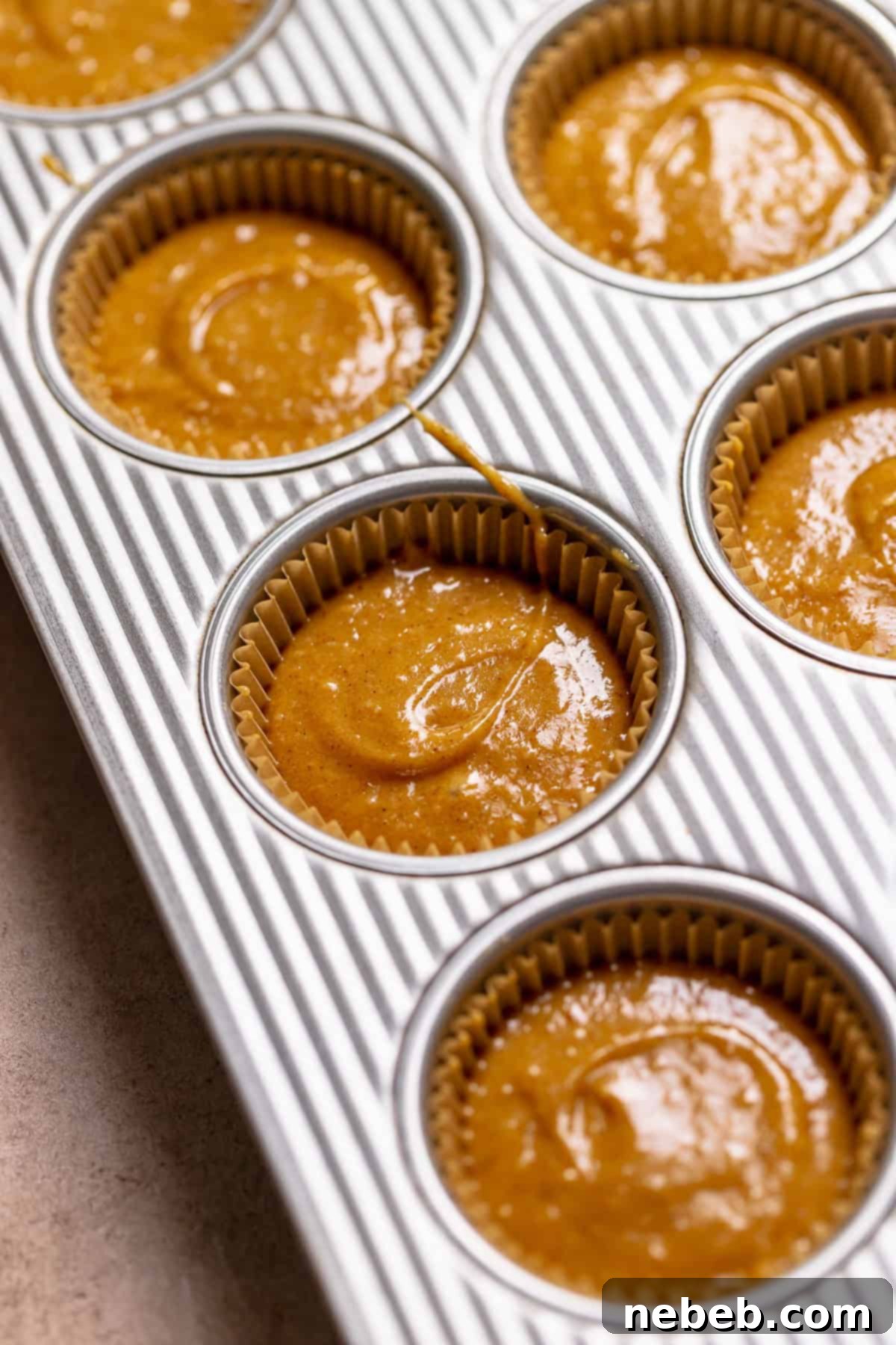 Pumpkin spice batter scooped into liners in a cupcake tray.