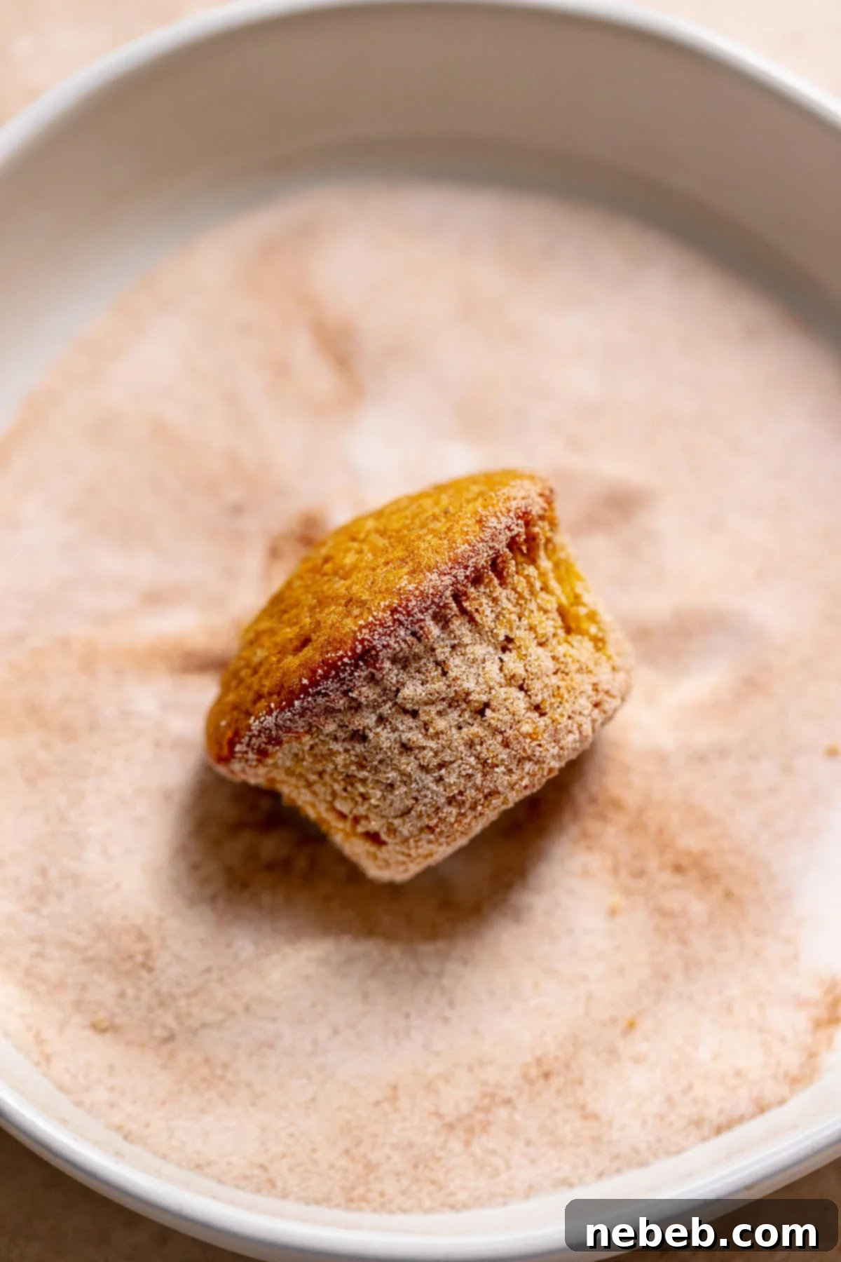 A pumpkin cupcake being rolled in spiced sugar.