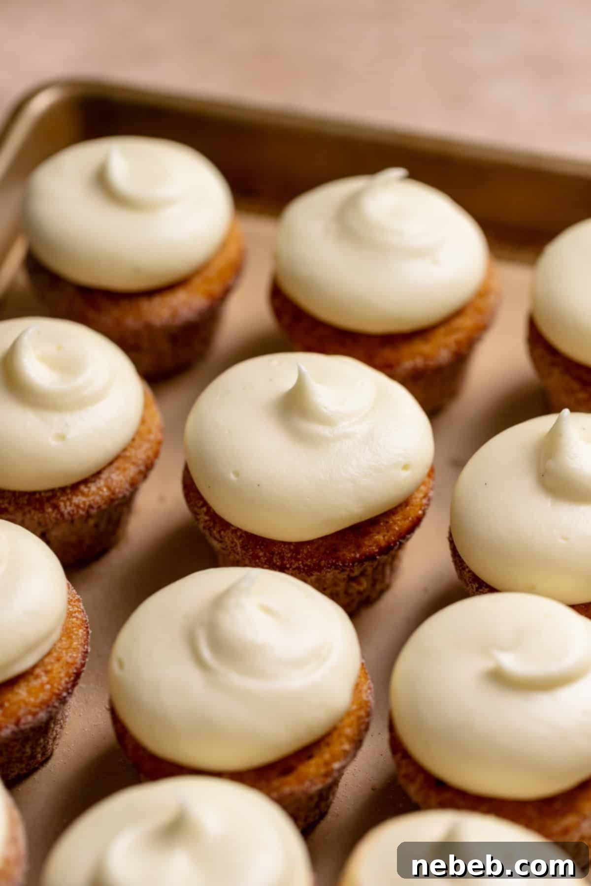 Cream cheese frosted pumpkin cupcakes on a baking tray.