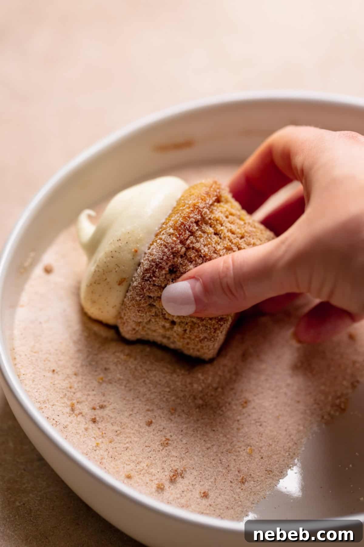 A hand rolling a pumpkin spice cupcake in sugar.