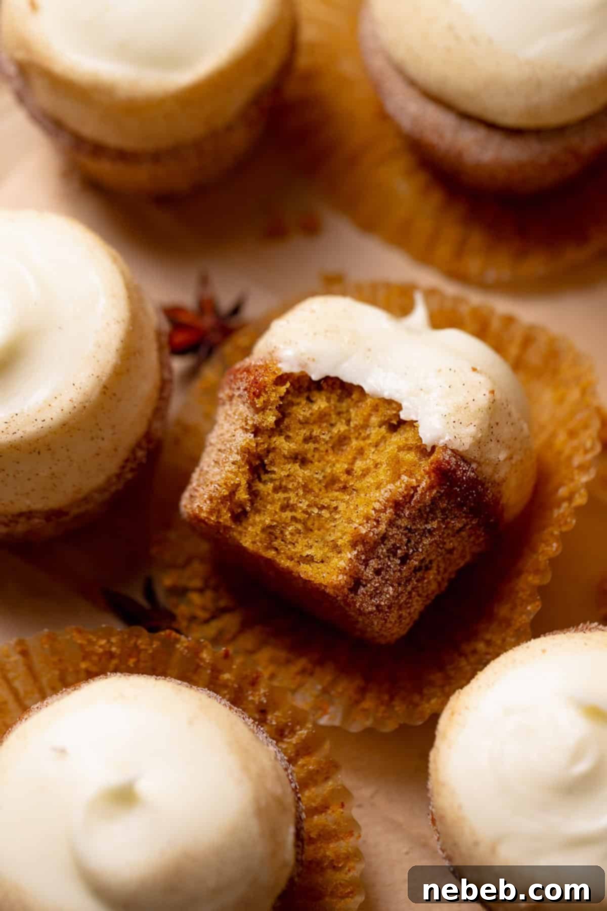 A pumpkin cupcake with cream cheese frosting on its side missing a bite.