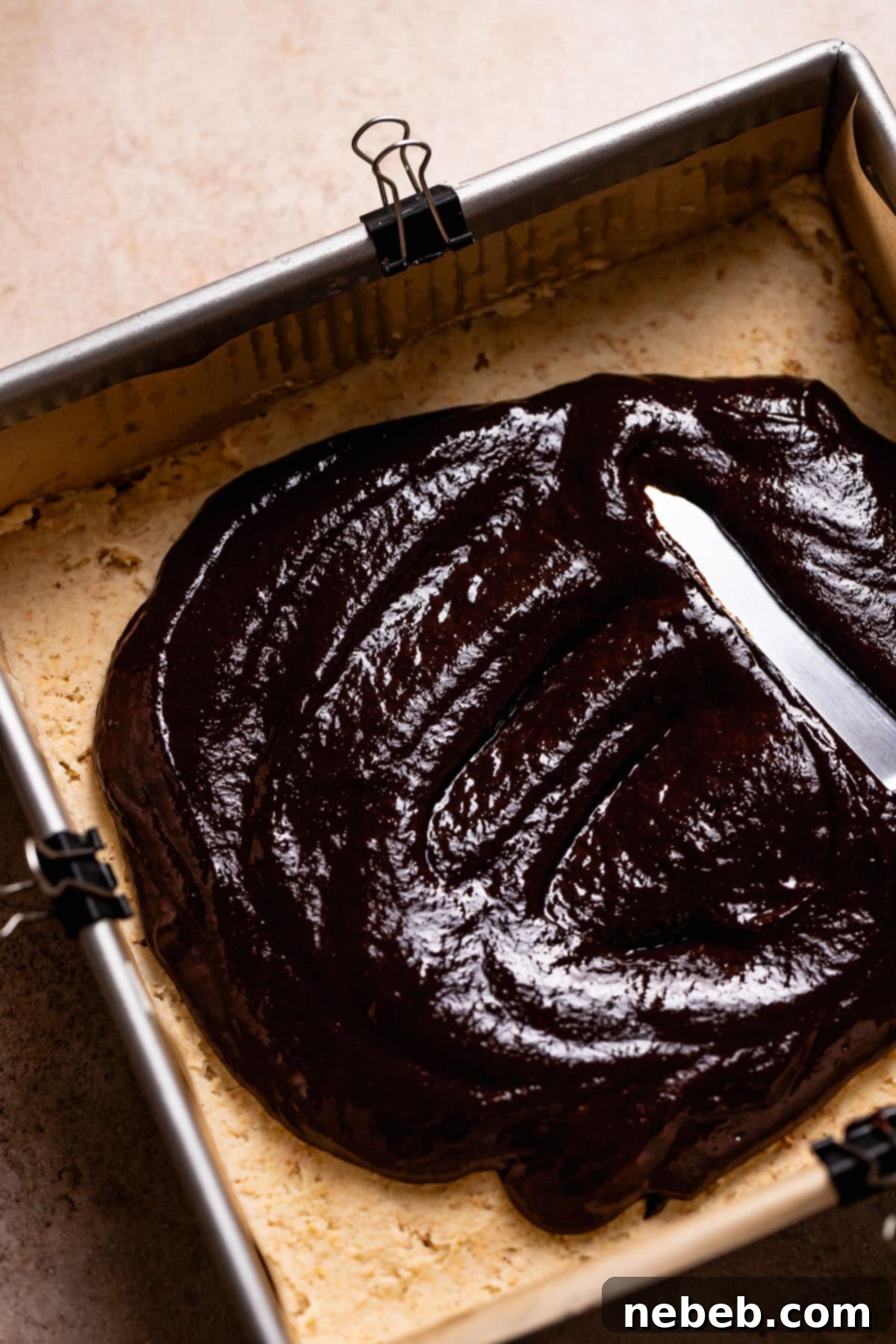 A metal spatula spreading the chocolate filling on top of the graham cracker cookie dough base.