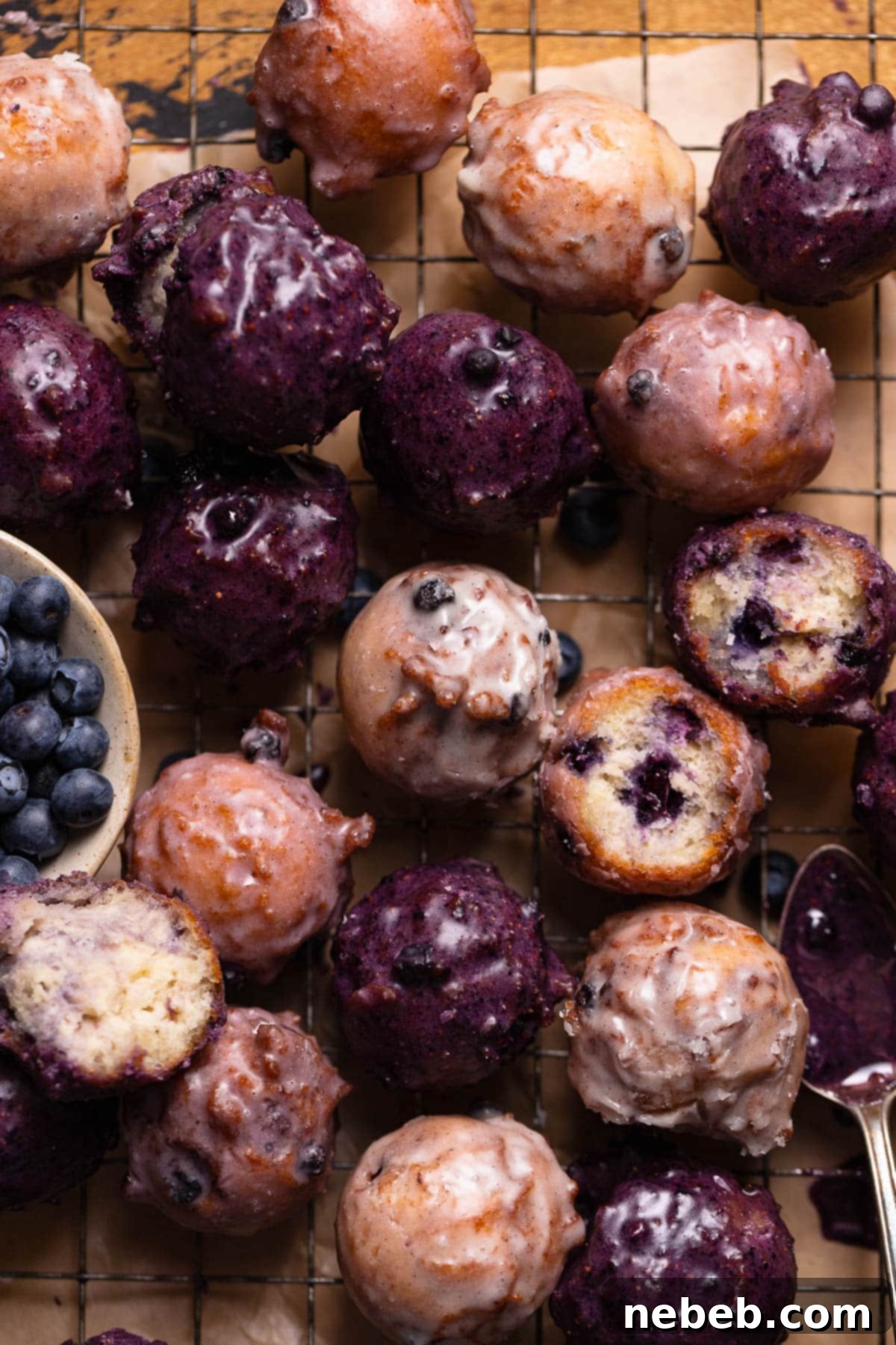 Mini blueberry cake donuts with blueberry glaze sitting in a pile on a wire rack.