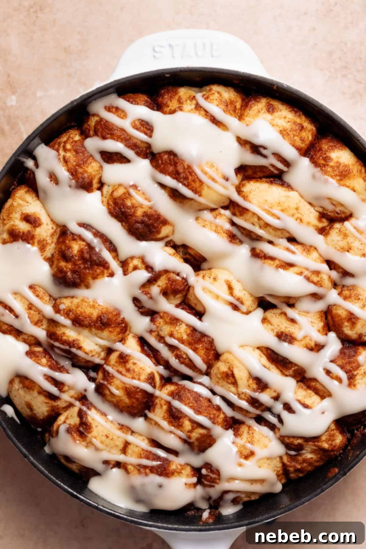 Cinnamon roll monkey bread in a skillet drizzled with cream cheese icing.
